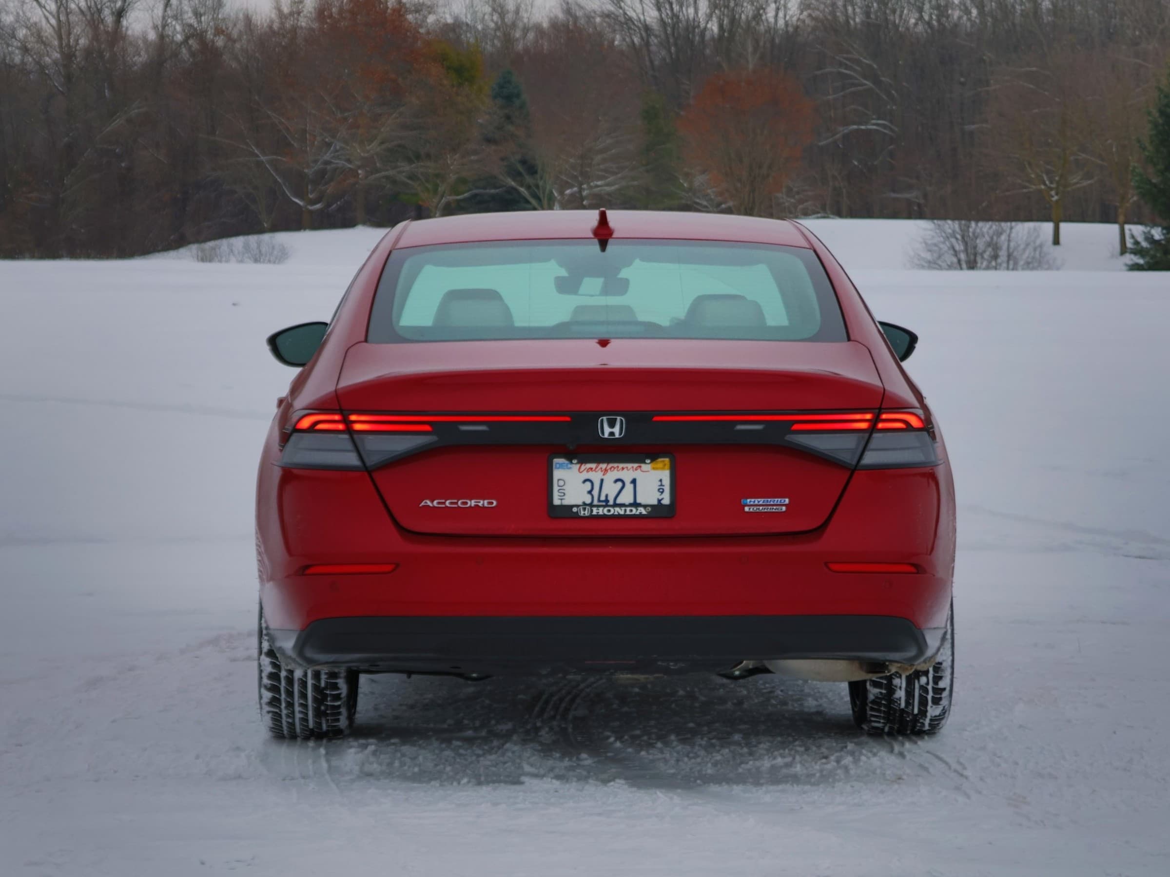 Straight-on rear view of a red Honda Accord Hybrid with full-width LED taillights and Accord and Hybrid Touring badges, parked on snow.