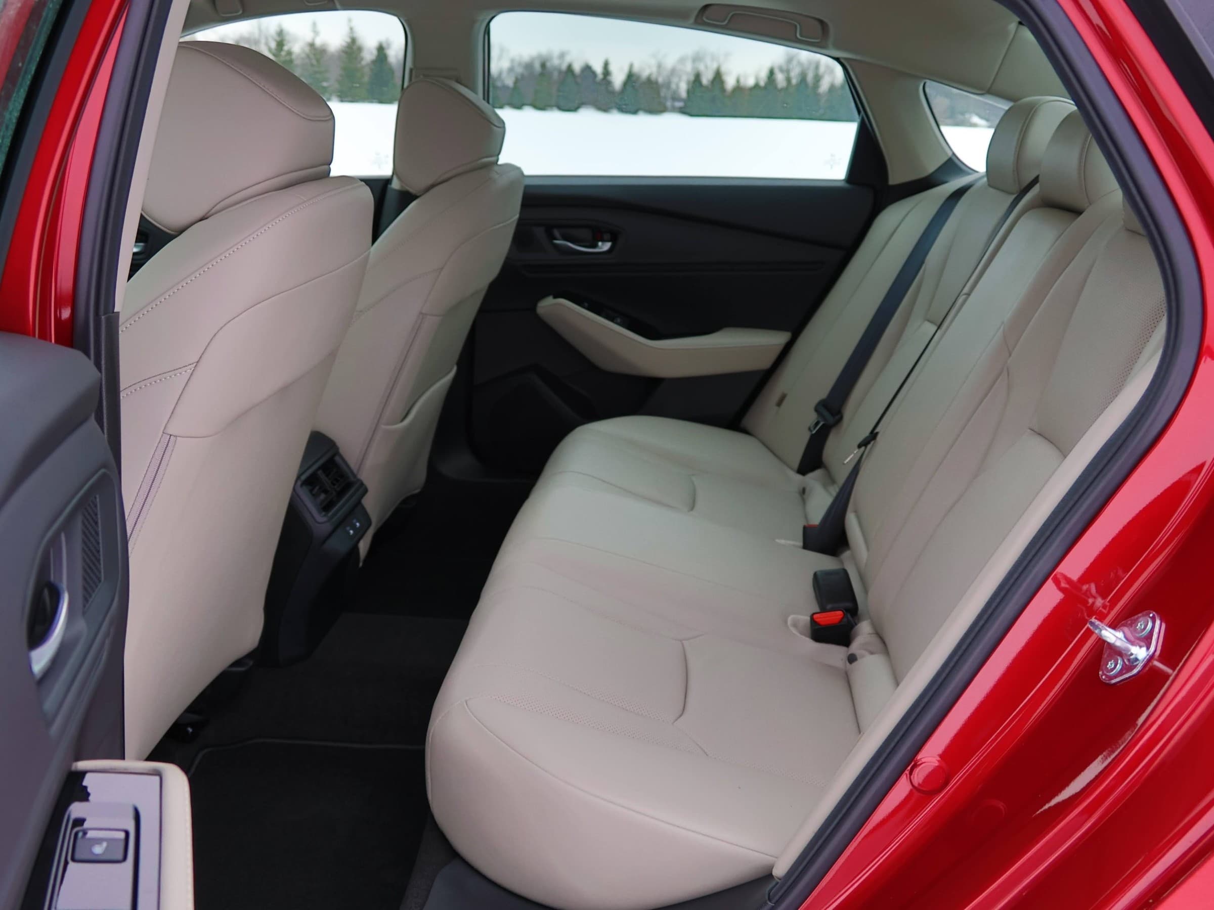 Rear bench seat of a Honda Accord Hybrid seen through the open back door, in light beige leather with rear air vents behind the center console.