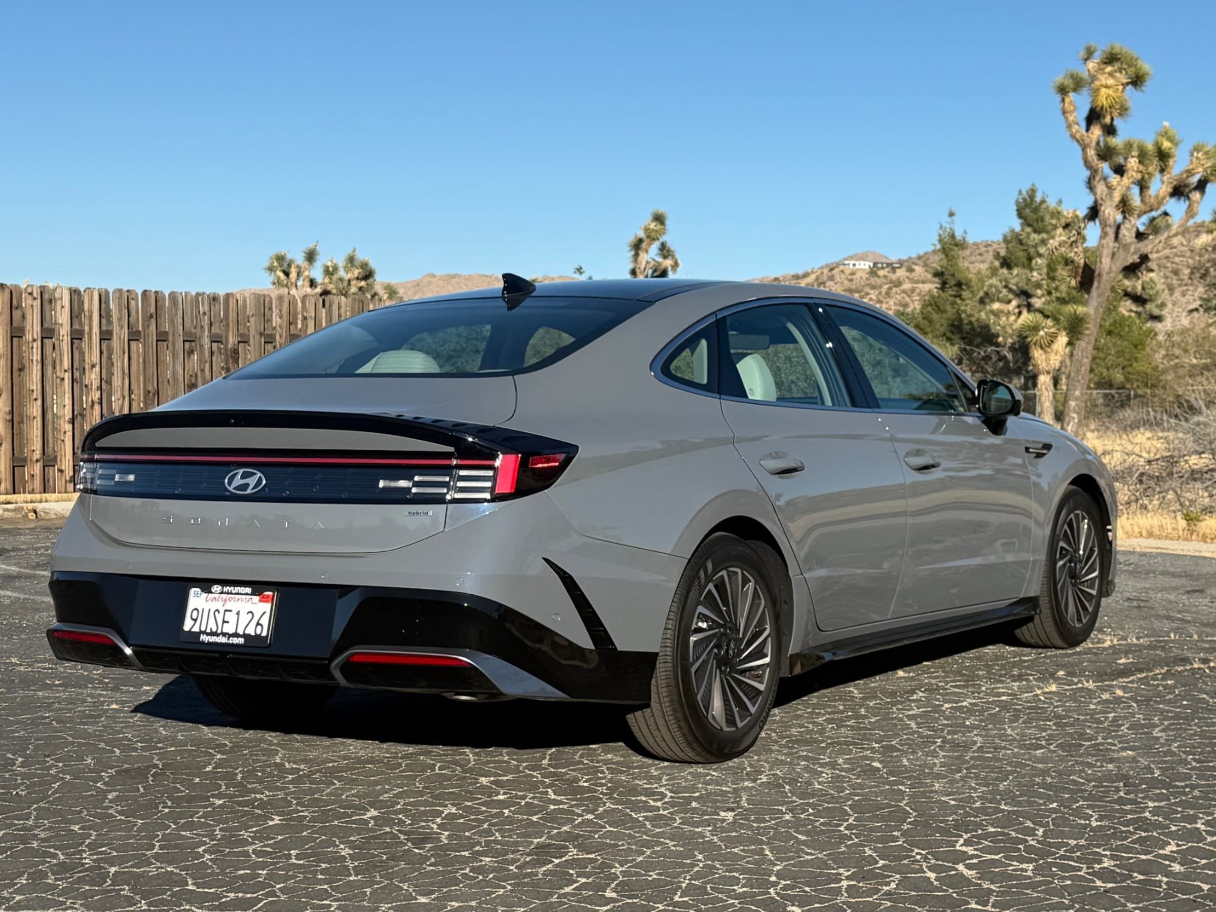 Rear three-quarter view of a gray Hyundai Sonata Hybrid showing its full-width taillight bar and black rear bumper, parked in the desert.