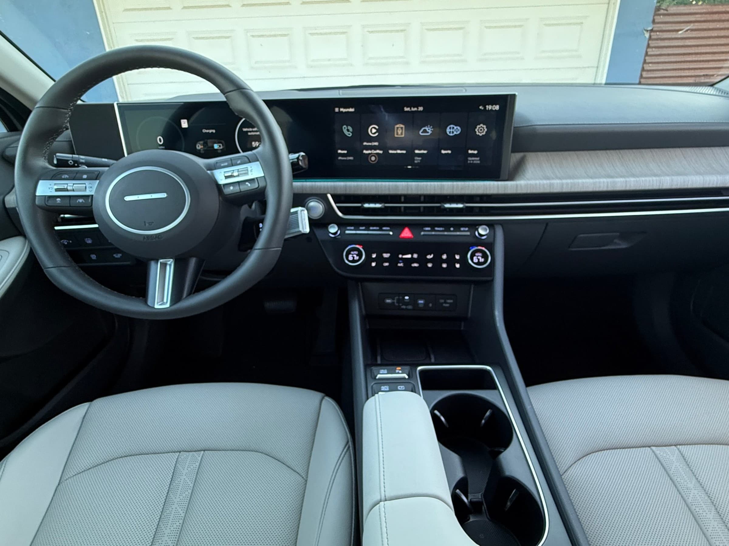 Hyundai Sonata Hybrid dashboard with a curved panoramic display, a steering wheel with a minimalist hub, climate controls and a light gray center console.