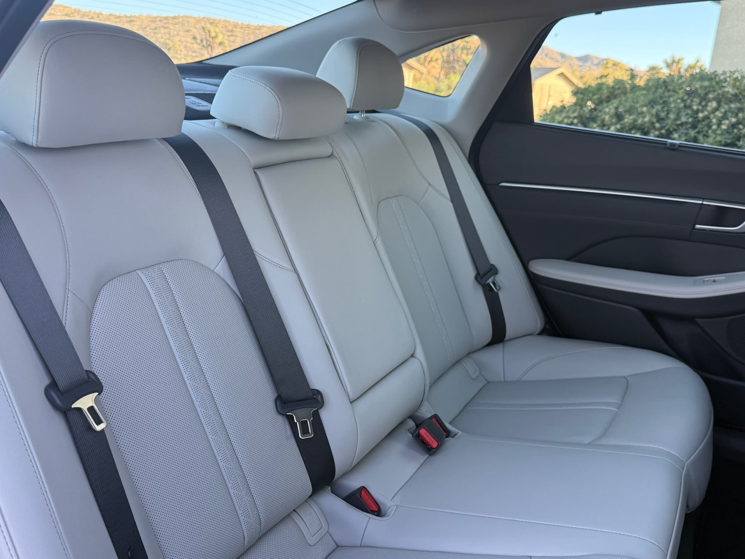 Rear bench seat of a Hyundai Sonata Hybrid in light gray perforated leather, with black seatbelts and dark door trim.