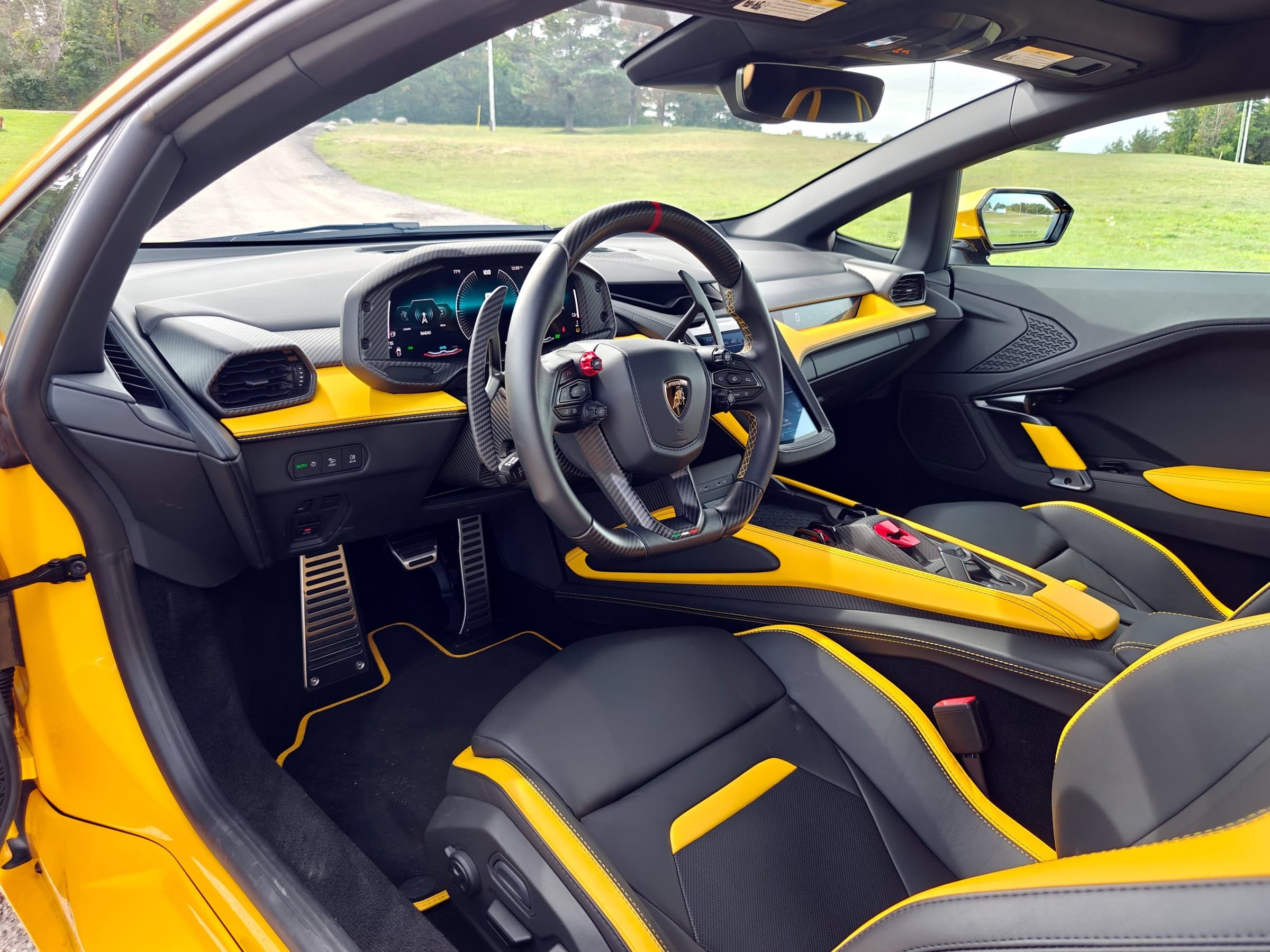 Lamborghini Temerario cockpit seen through the open driver’s door, with a carbon fiber steering wheel, digital gauges and black seats with yellow accents.
