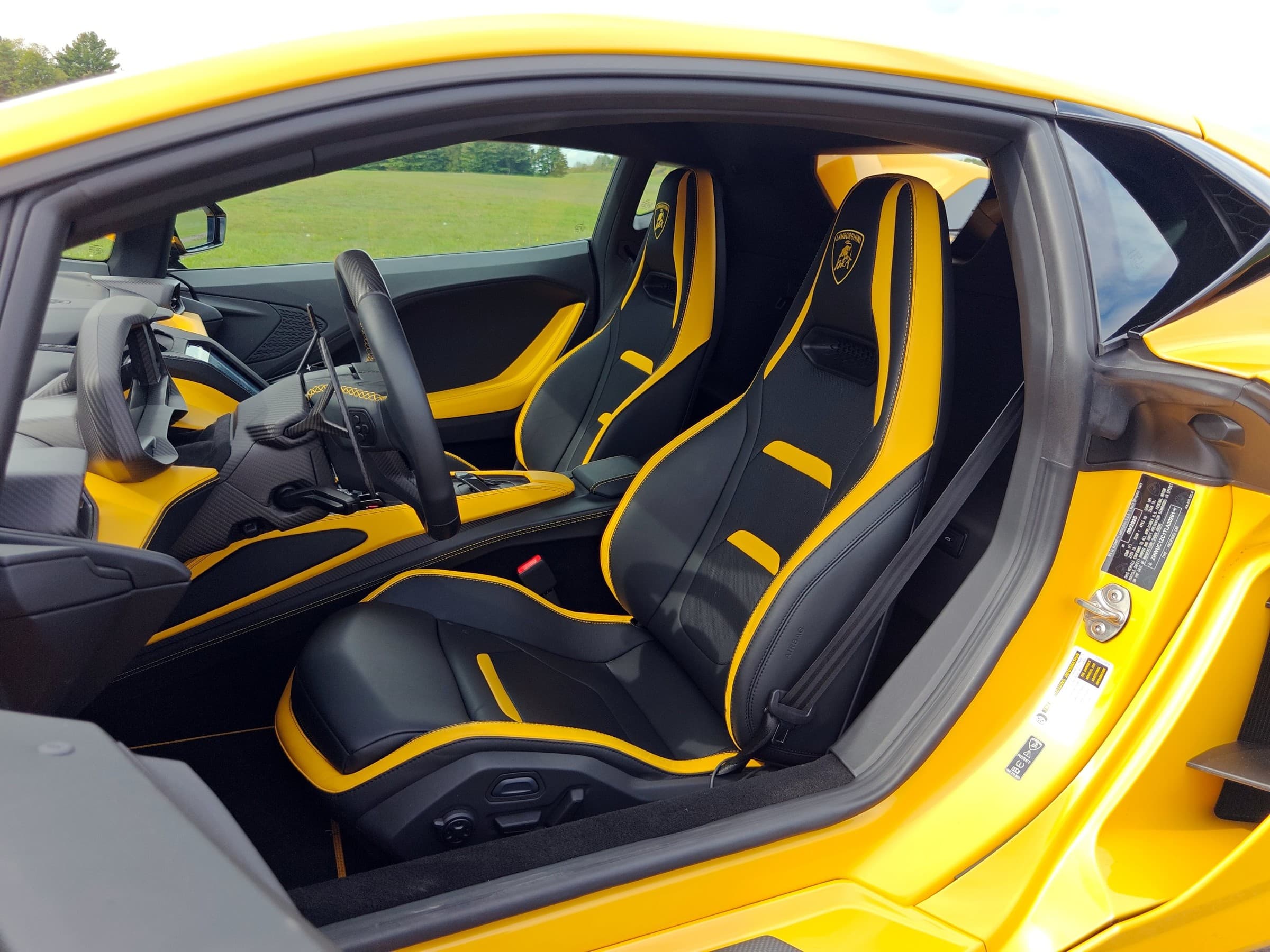 Lamborghini Temerario cabin seen through the open driver’s door, showing black sport seats with yellow trim, a carbon fiber steering wheel and a yellow-accented center console.