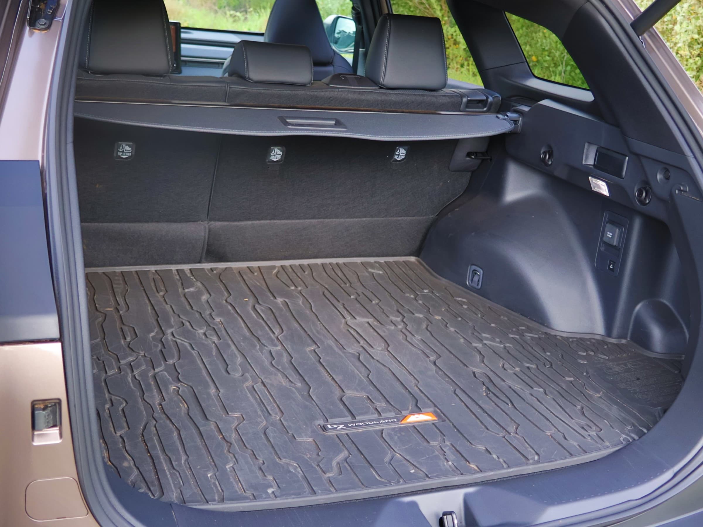 Cargo area of a Toyota bZ Woodland with a rugged rubber cargo mat bearing a bZ Woodland logo, a retractable cargo cover and upright rear seats.