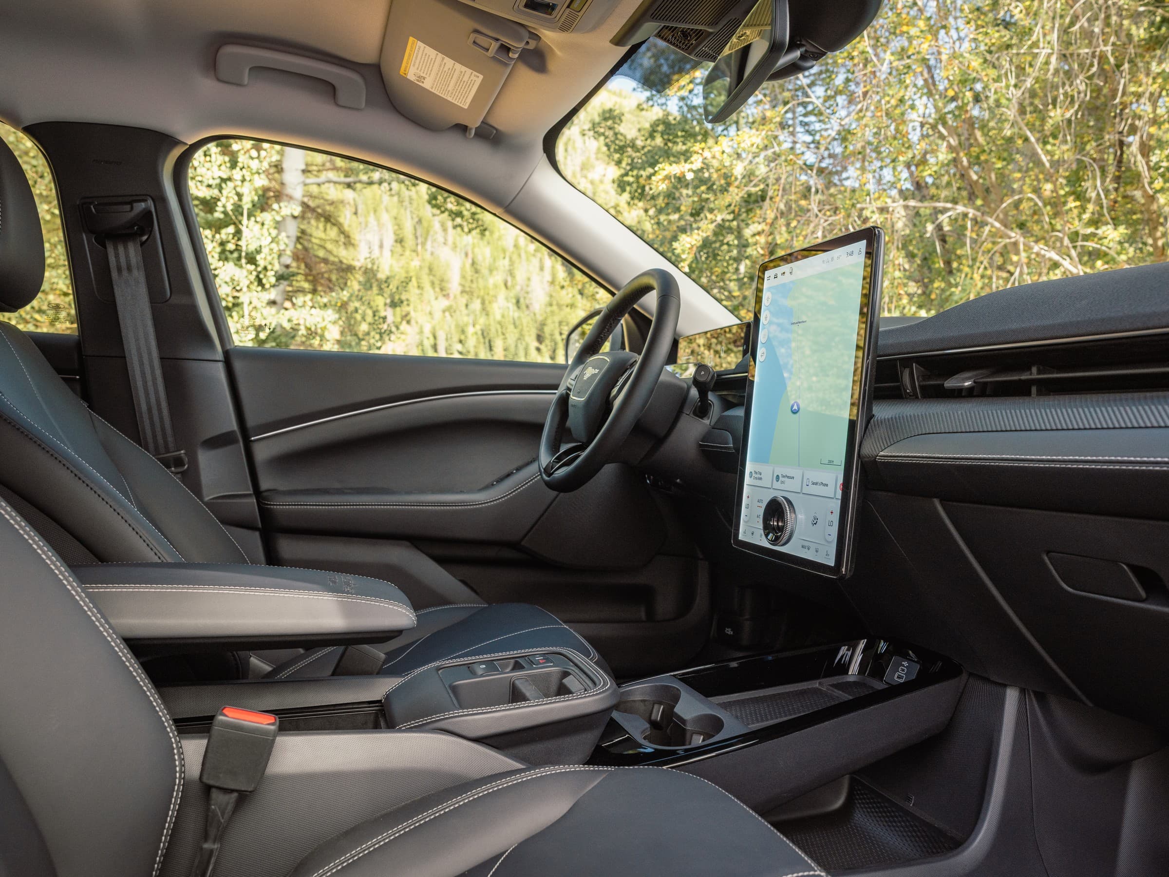 Ford Mustang Mach-E Trail cabin seen from the passenger side, with black leather seats, a large portrait-style center touchscreen showing a map and a floating center console.