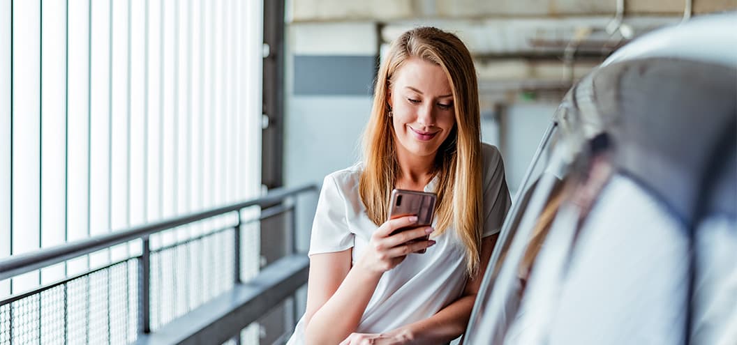 Woman smiling and standing against car looking at phone
