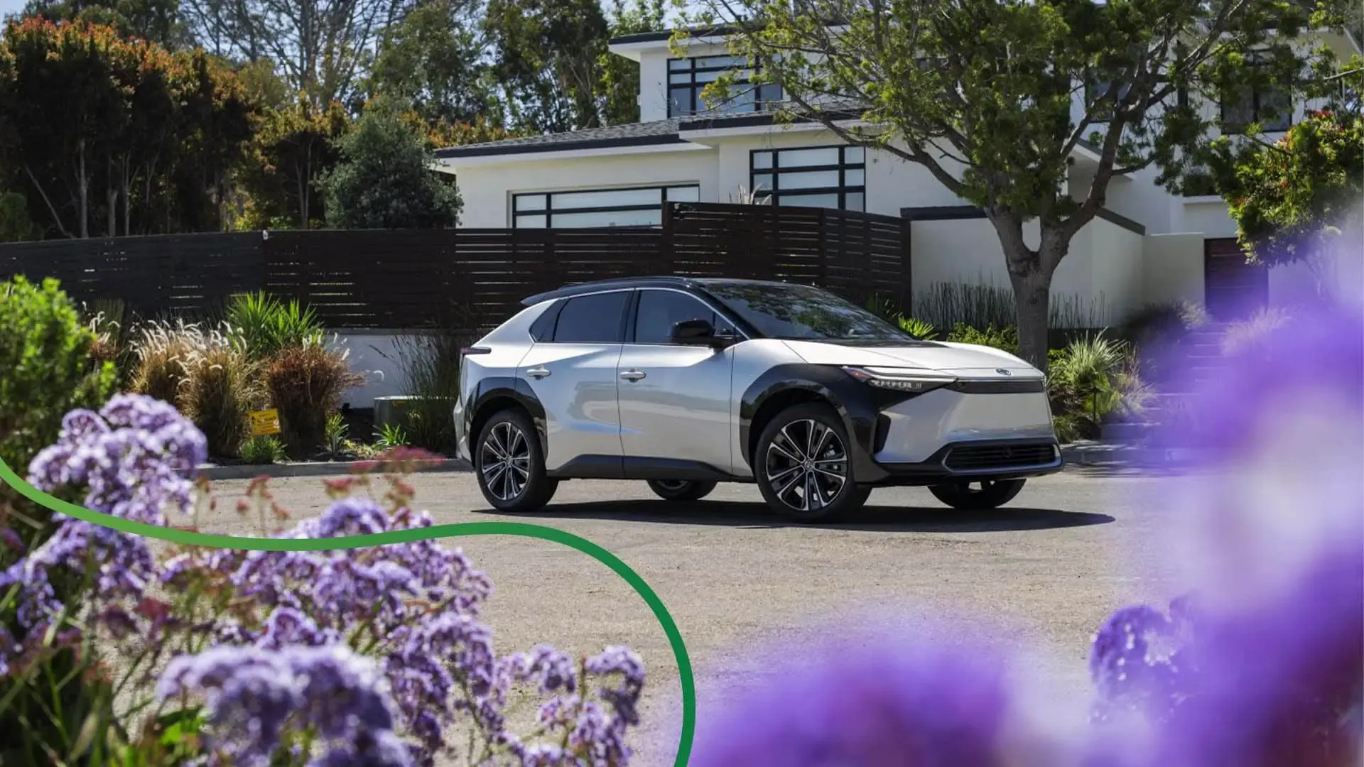 Toyota bZ4x in front of modern house with purple flowers in foreground