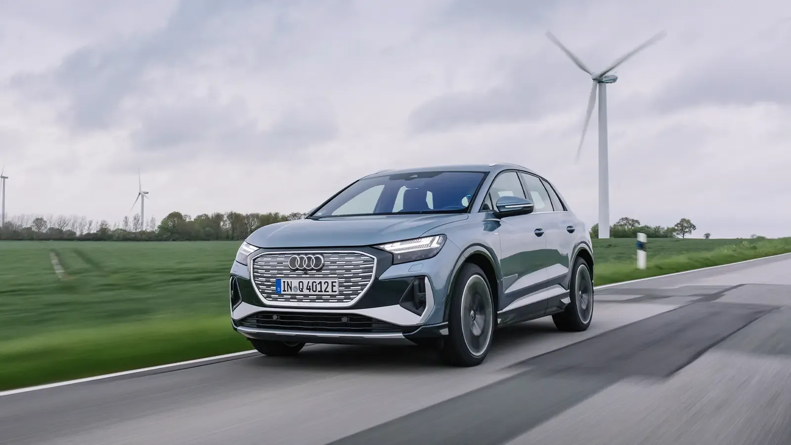 audi q4 e-tron suv driving on a paved road with a green grassy field in the background
