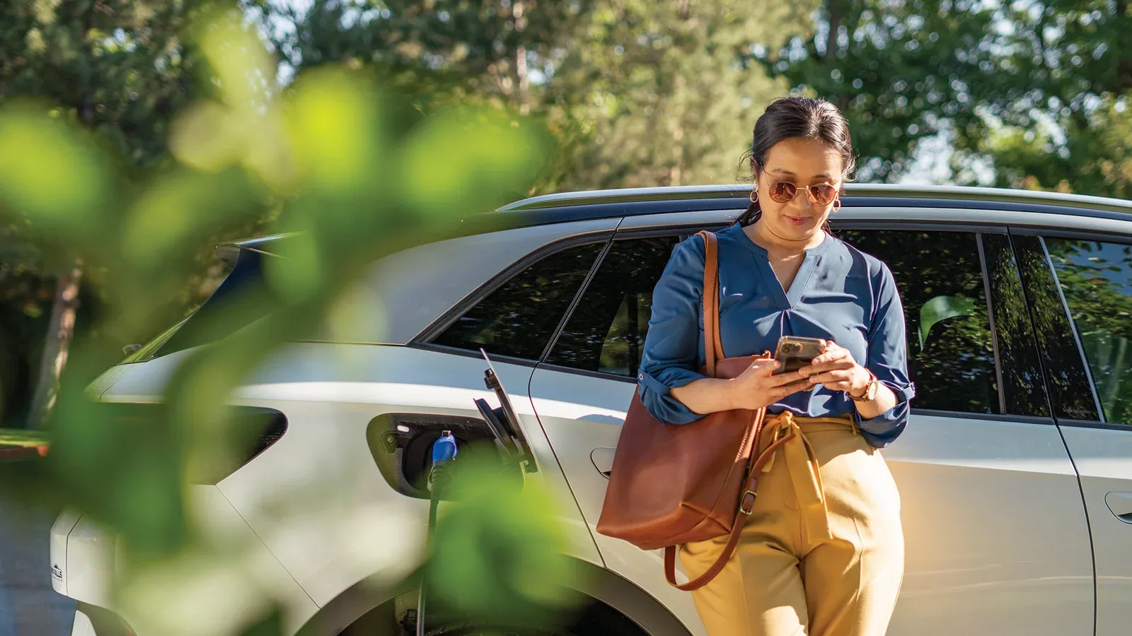 A woman standing next to her EV charging while looking at her phone