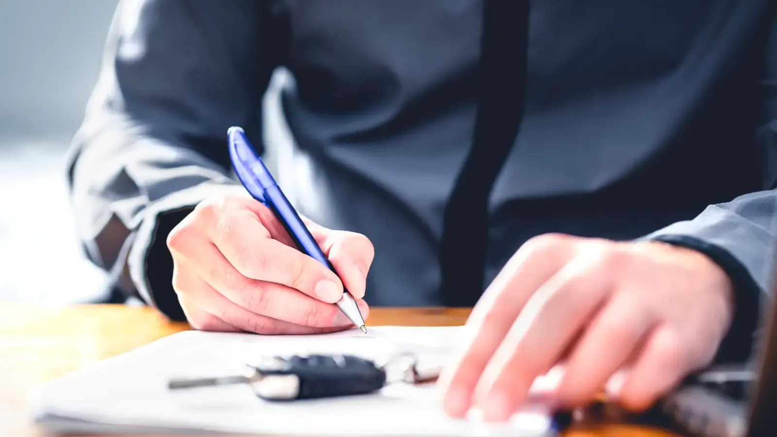 Person signing document with car keys on top of paperwork 