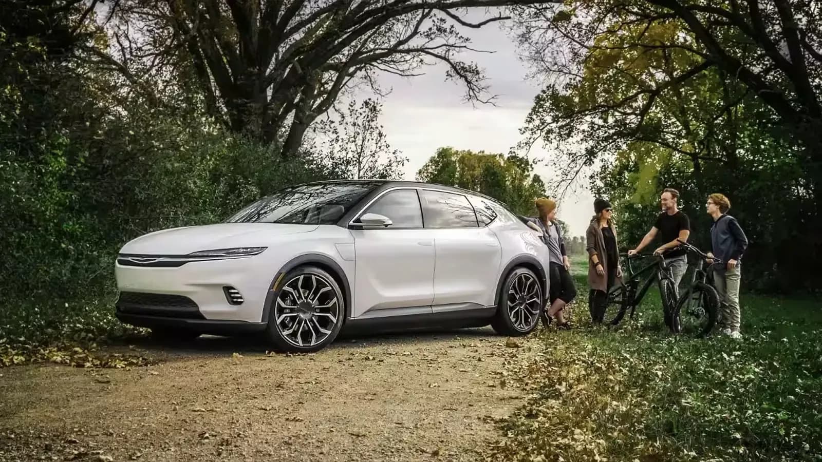 A group of young adults, hikers and mountain bike riders talking beside a Chrysler Airflow concept vehicle parked along a park trail