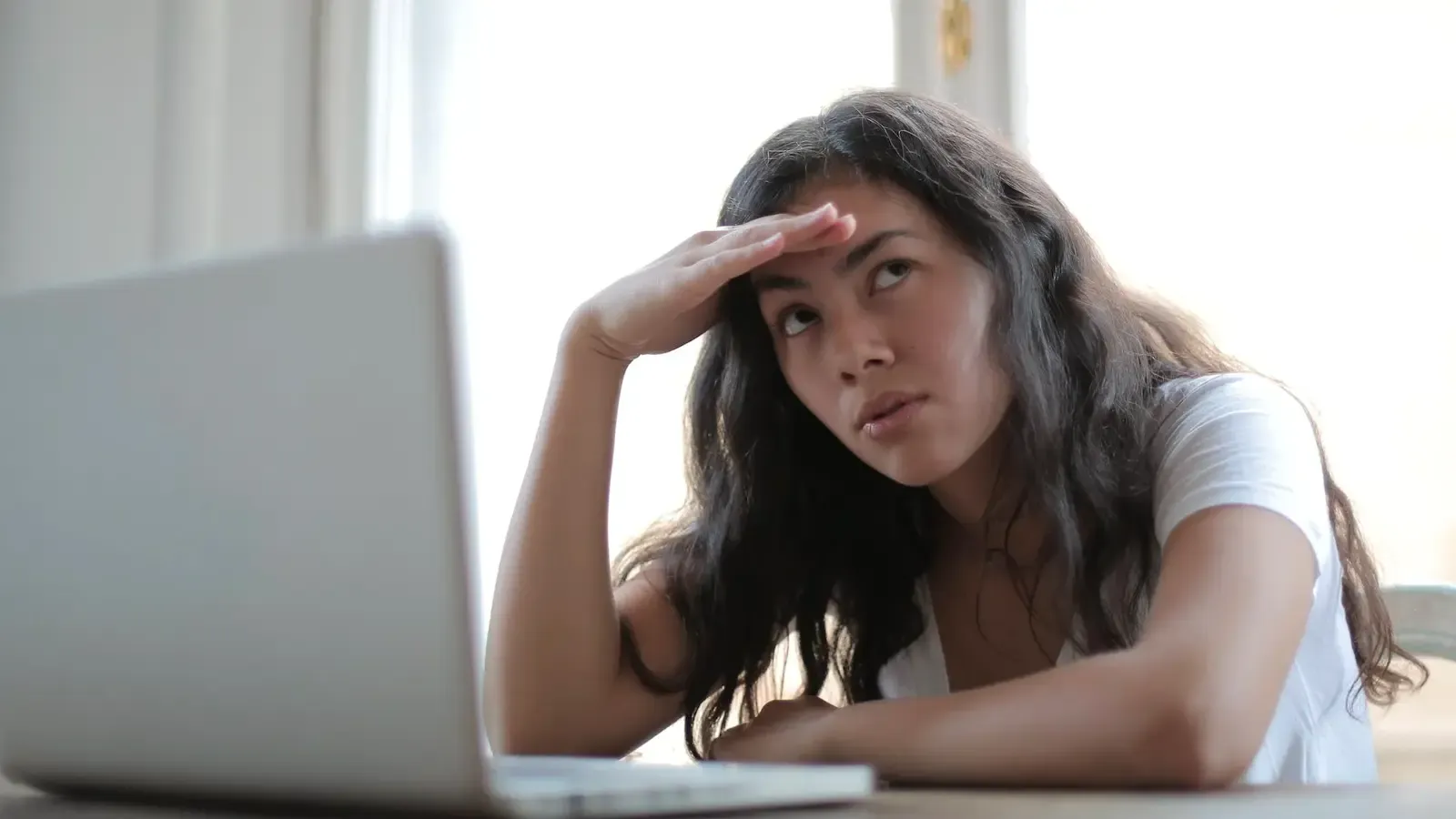 Woman sitting by her laptop, confused and frustrated 