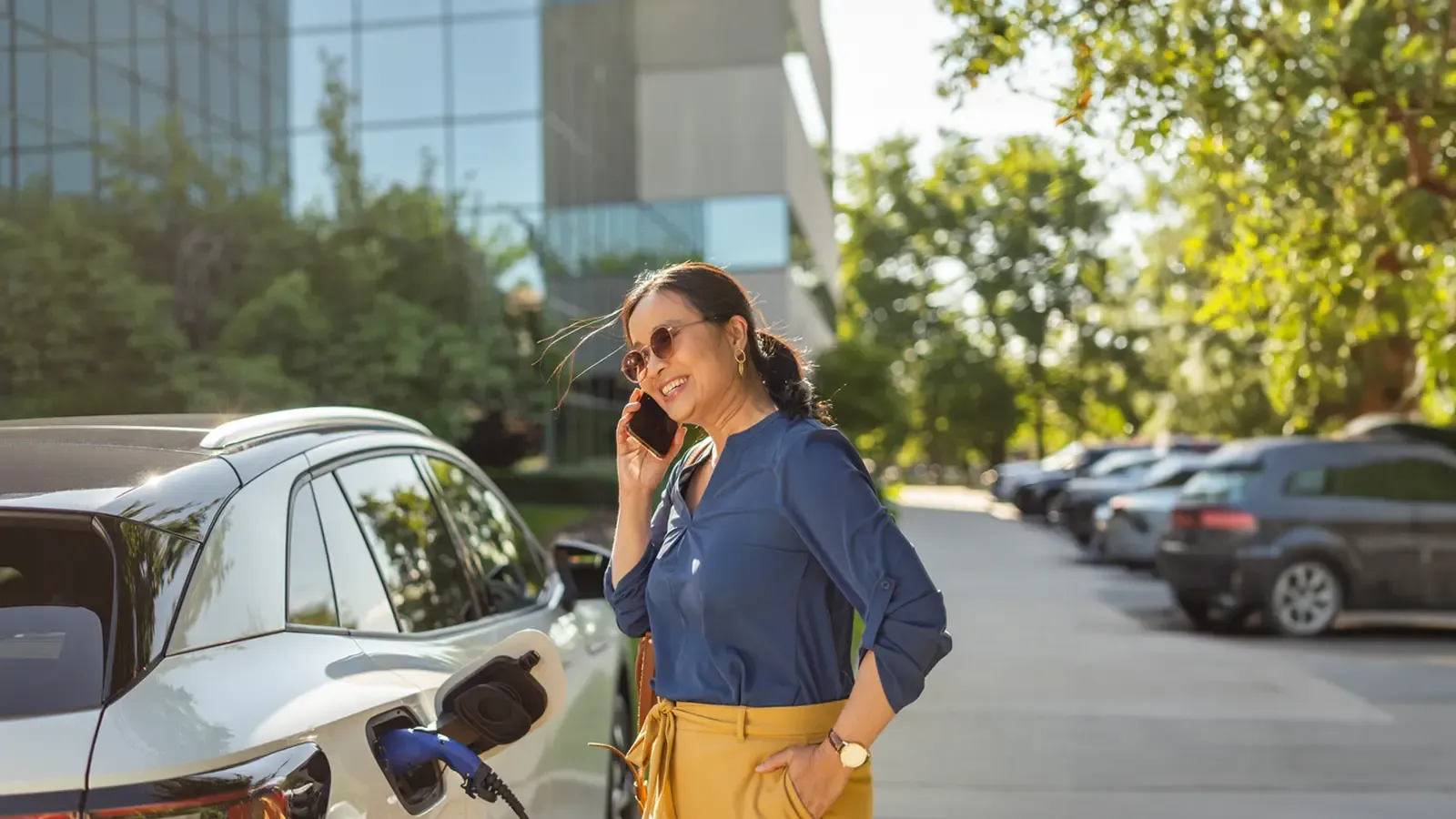 Woman standing by office building on her phone as her car charges 