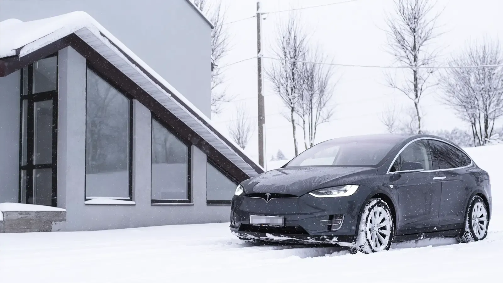 Tesla Model X parked by a house in snowy conditions