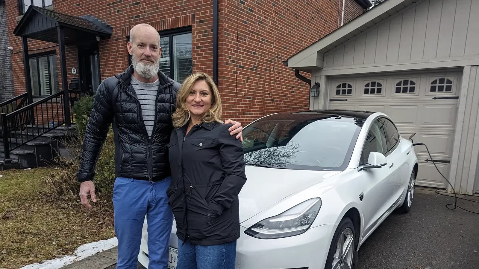 A couple, Bruce and Marlene, standing in front of their Tesla electric vehicle