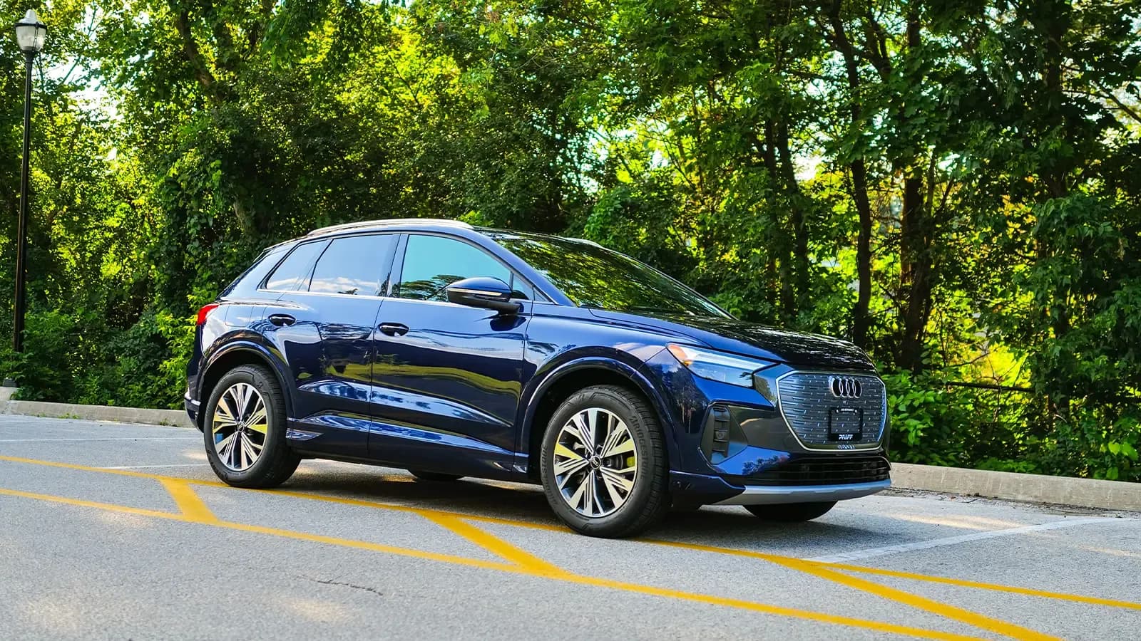 Blue Audi q4 e-tron parked in front of many lush, green trees.