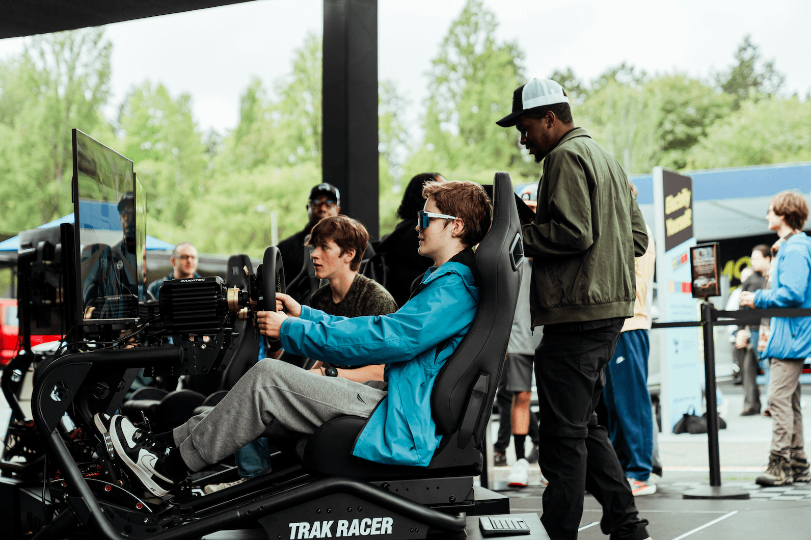 Two people use a TRAK RACER driving simulator at an outdoor event.