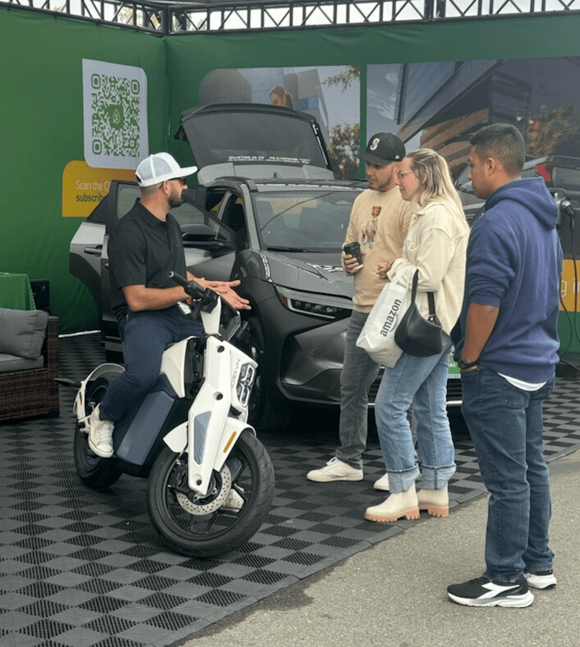A person on an electric scooter talks with three people beside a gray SUV with its hatch open.