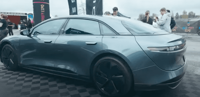 Side view of a blue electric sedan on display at an outdoor expo.