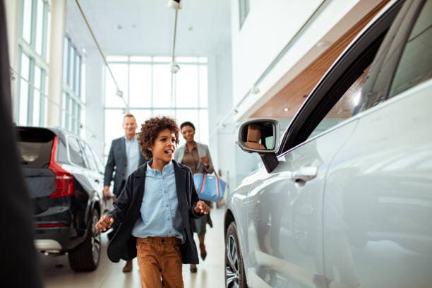 Child at Car Dealership with Parents in Background