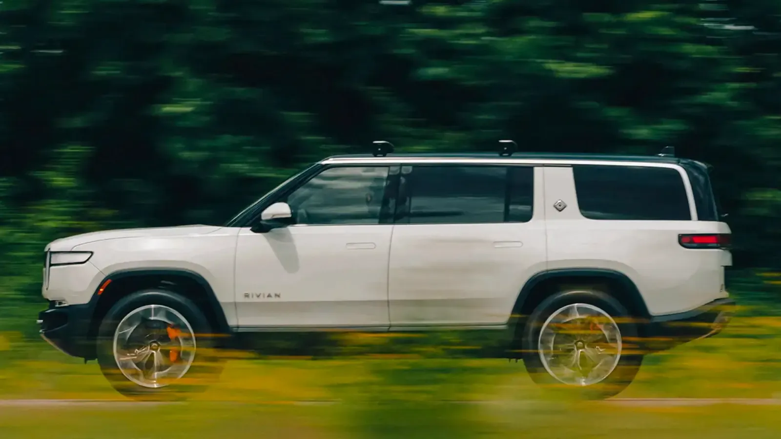 Rivian R1S driving on a grassy plain. It is an exterior view of the side profile 