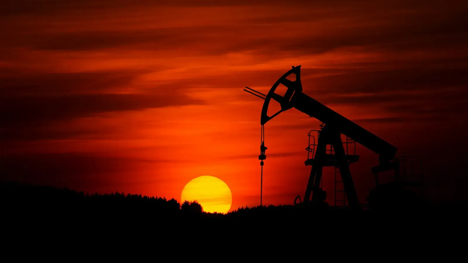 A beautiful red setting sun over an oil pump somewhere on planet earth signifying the reduction in reliance on this fossil fuel