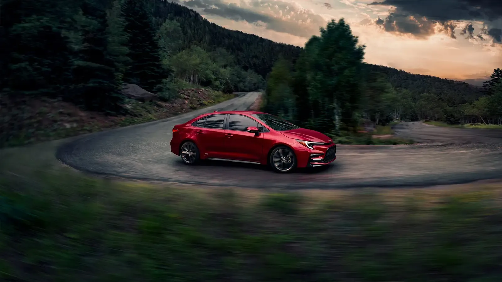 A red 2025 Toyota Corolla hybrid on a winding mountain road