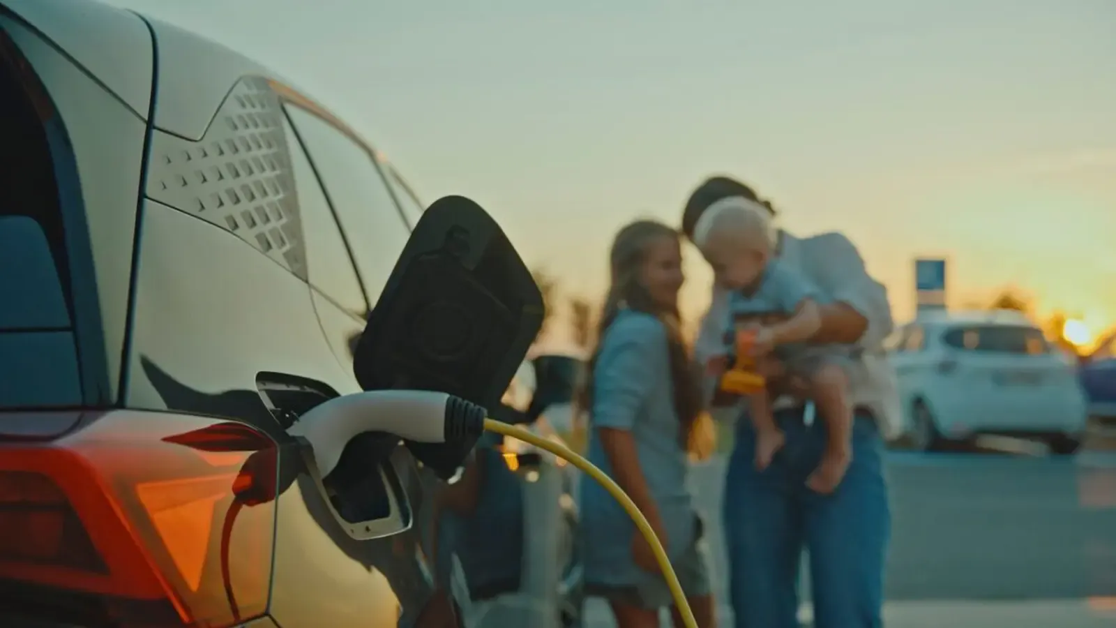 A happy family in the foreground at the beach while an EV charges