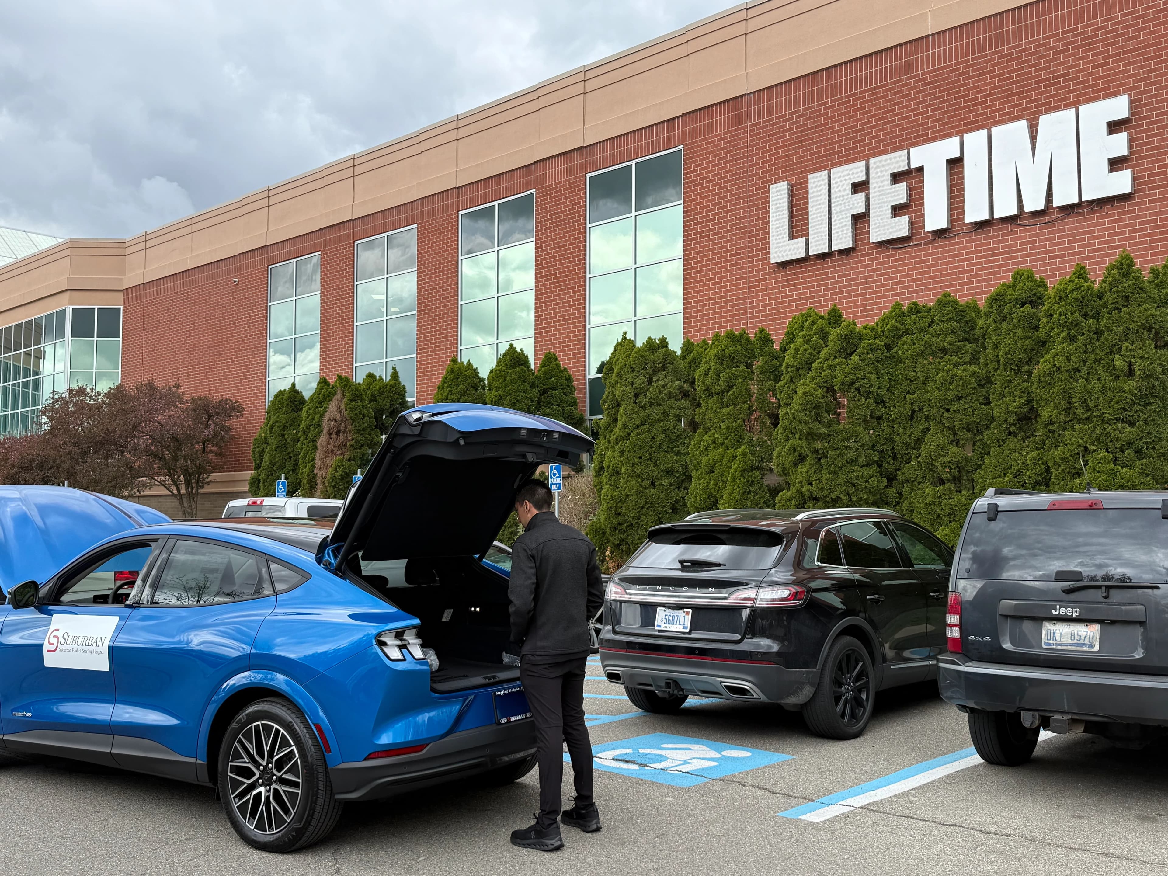 Vista trasera de tres cuartos de un Mustang Mach-E azul con la compuerta abierta en un estacionamiento de Lifetime.