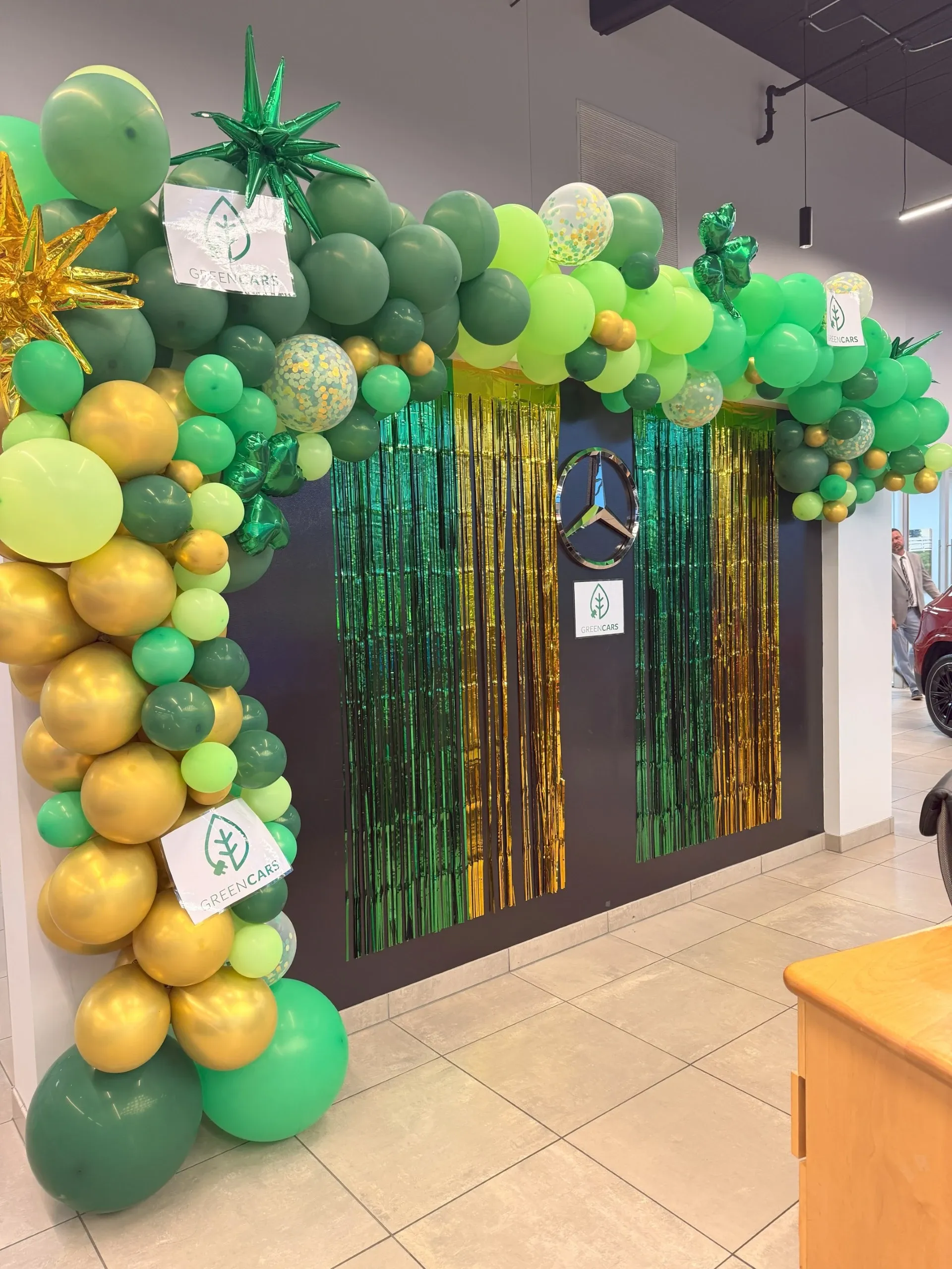 Un arco de globos con letreros de GreenCars y el emblema de Mercedes-Benz en una sala de exhibición.