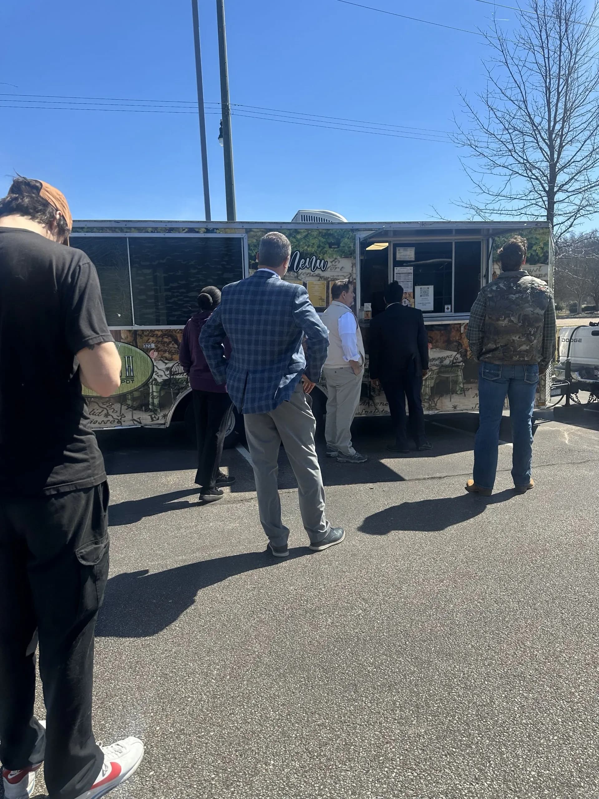 Varias personas hacen fila en un food truck bajo un cielo azul despejado.