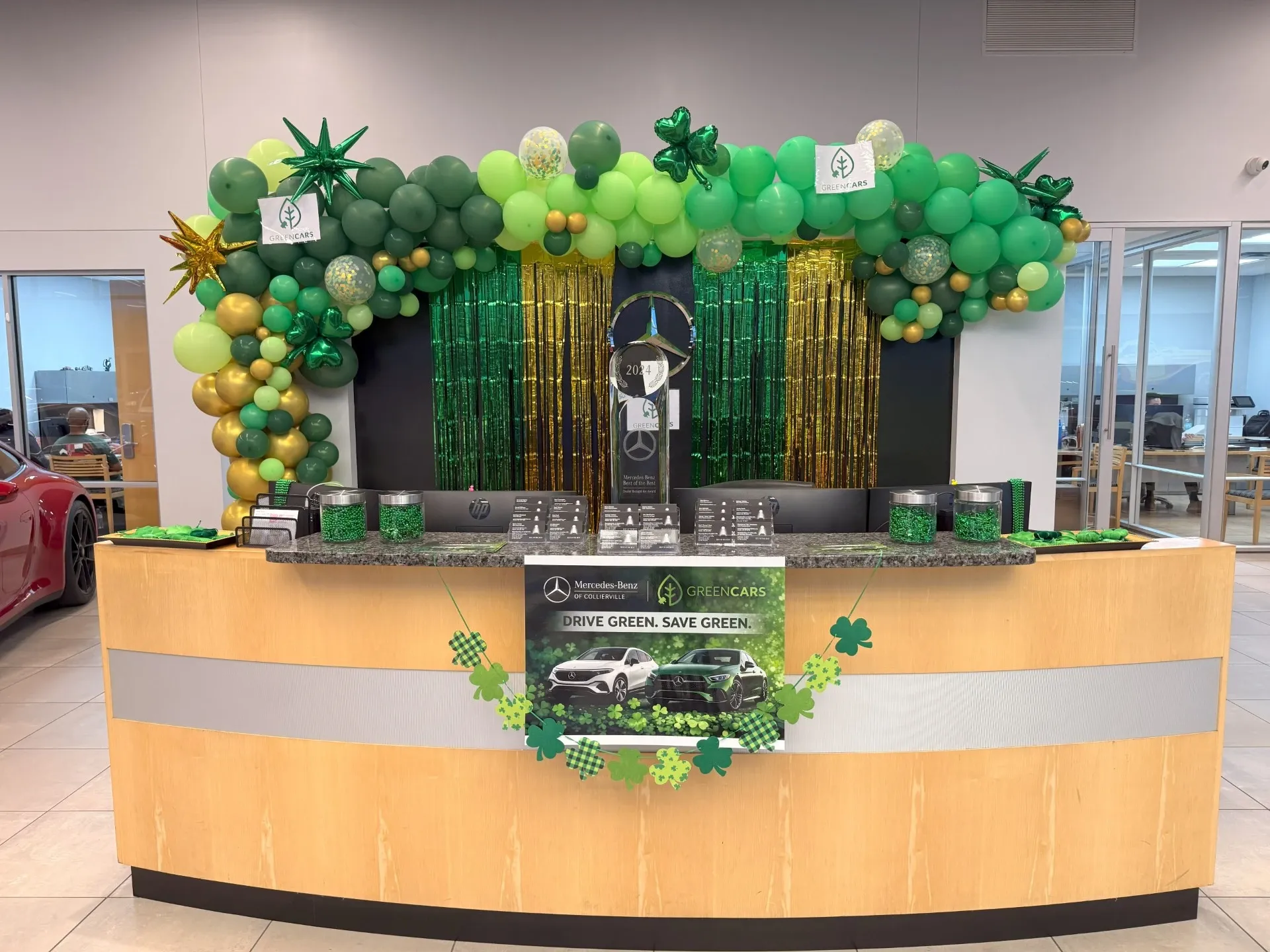 Mostrador de concesionario decorado con globos verdes, tiras brillantes y un letrero de Mercedes-Benz.