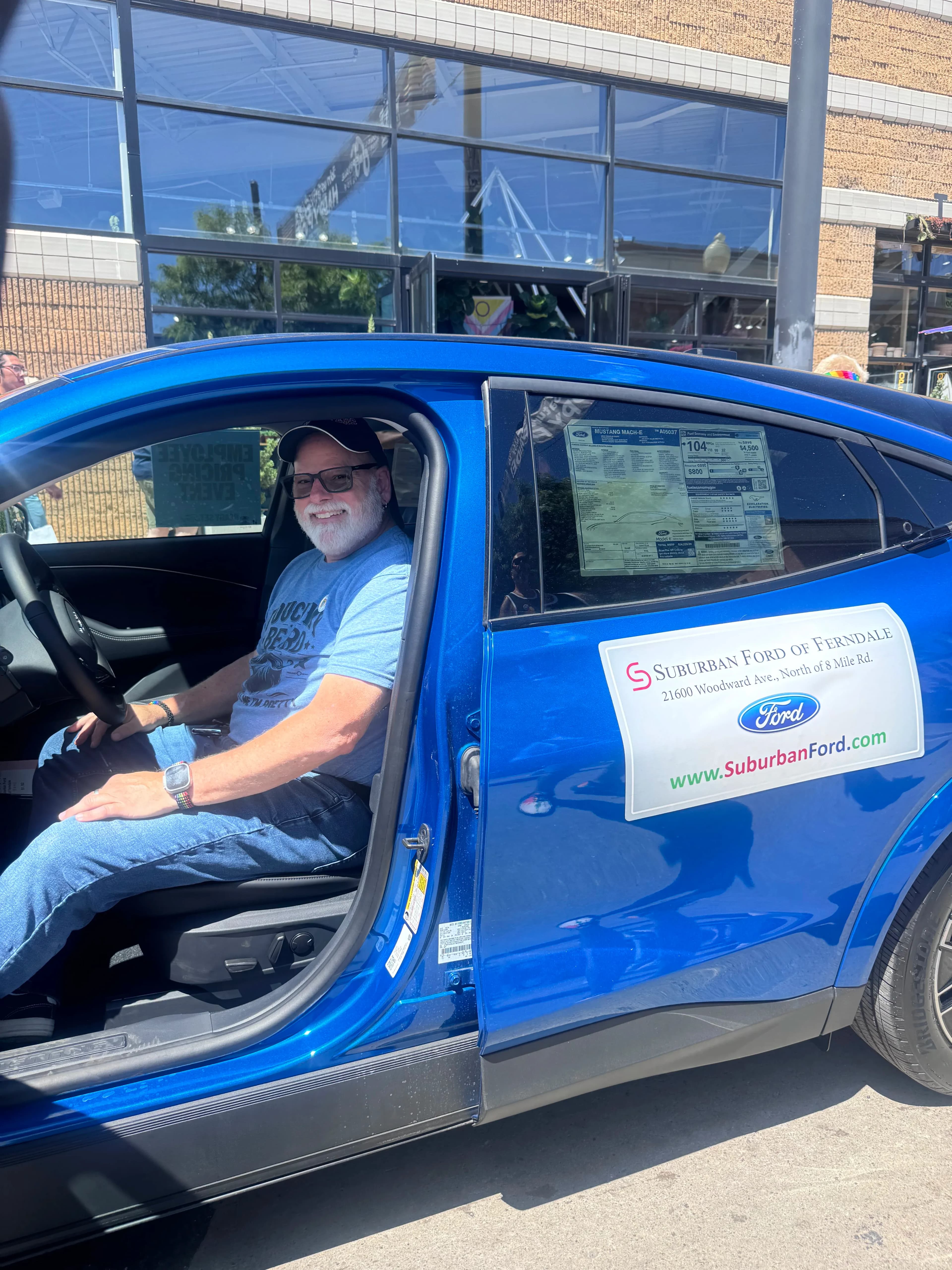 A person sits in the driver’s seat of a blue Ford Mustang Mach-E with the door open.