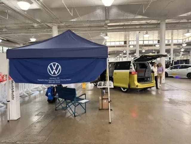 Una carpa de Volkswagen junto a una ID. Buzz amarilla con la puerta trasera abierta en un evento interior.