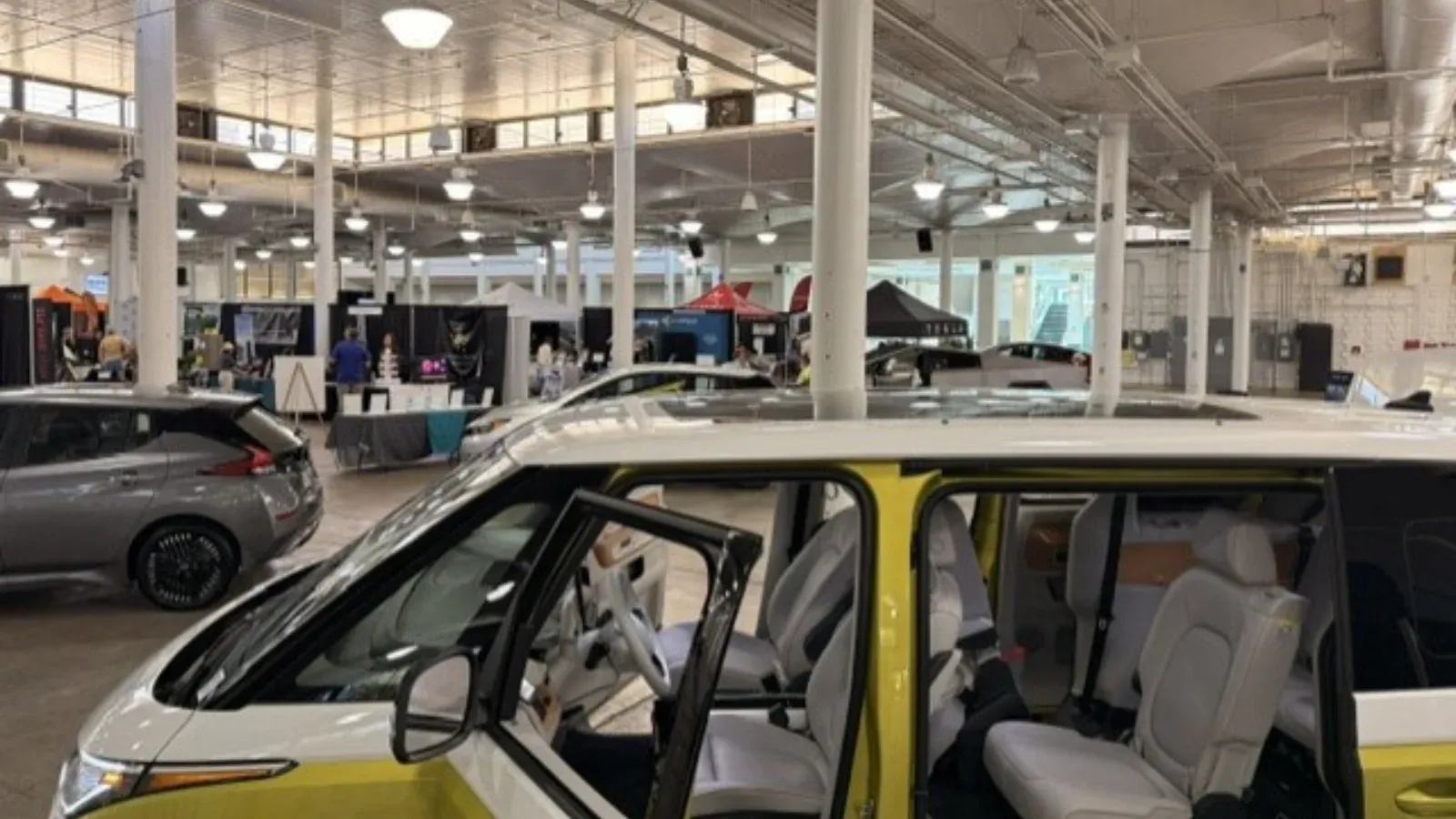 Puerta lateral abierta de una Volkswagen ID. Buzz amarilla y blanca en una feria interior de vehículos eléctricos.