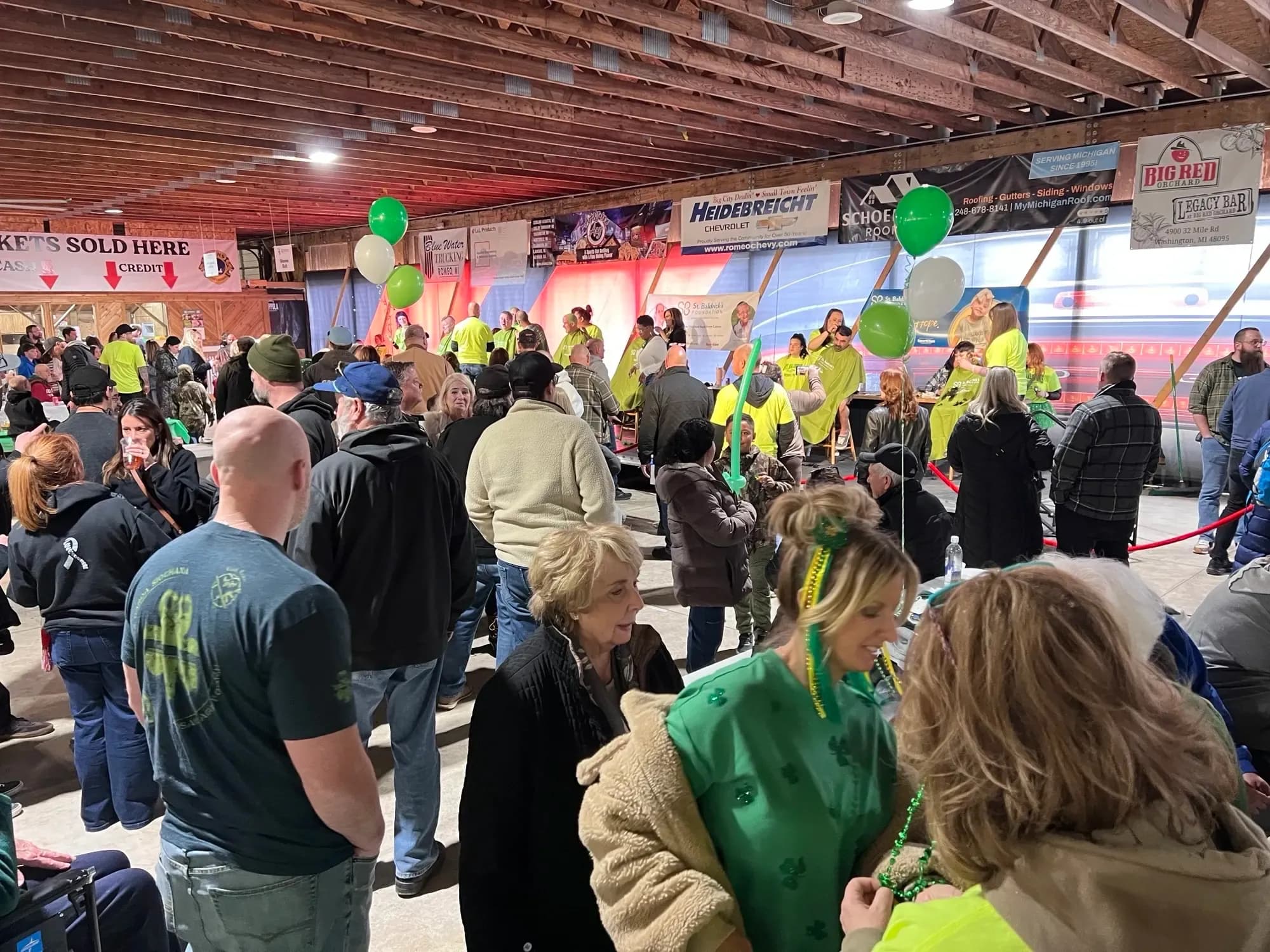 Crowd gathered indoors around tables and a stage at a St. Baldrick’s fundraiser.