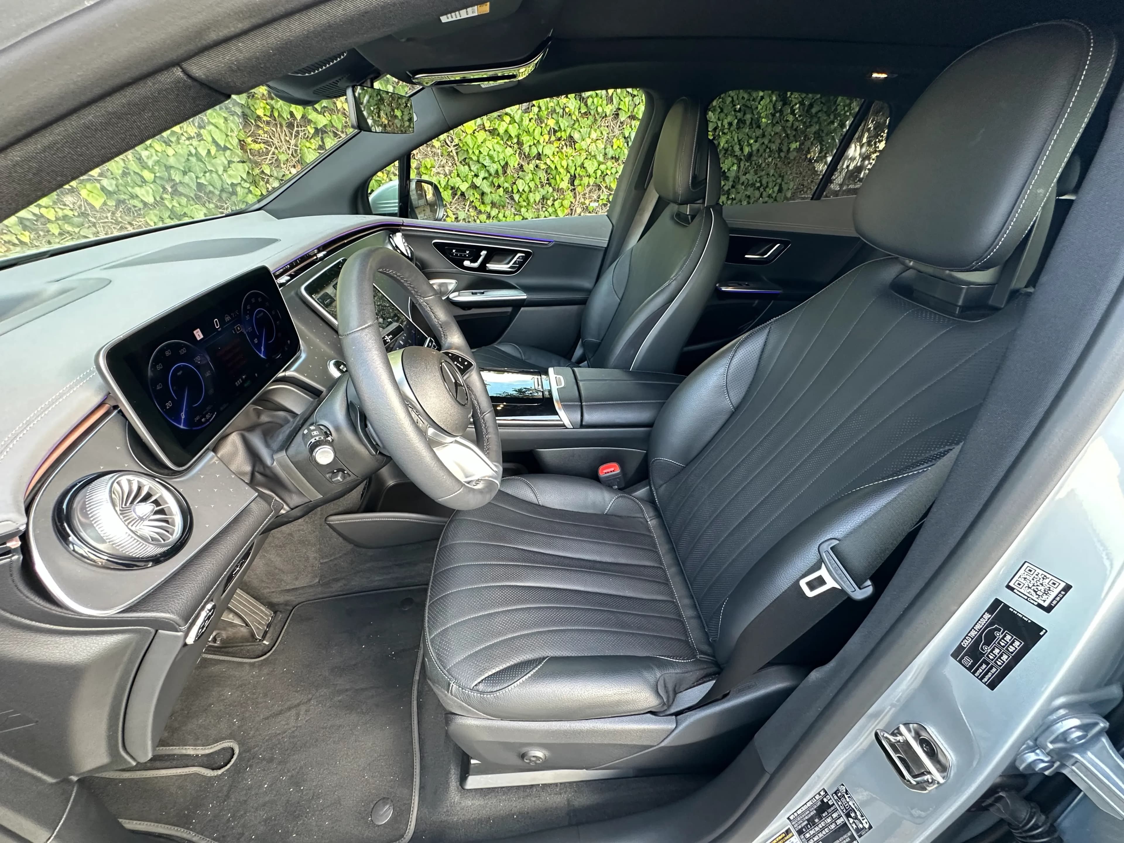 Front cabin of a Mercedes-Benz EQE SUV with black leather seats, digital displays, and ambient lighting.