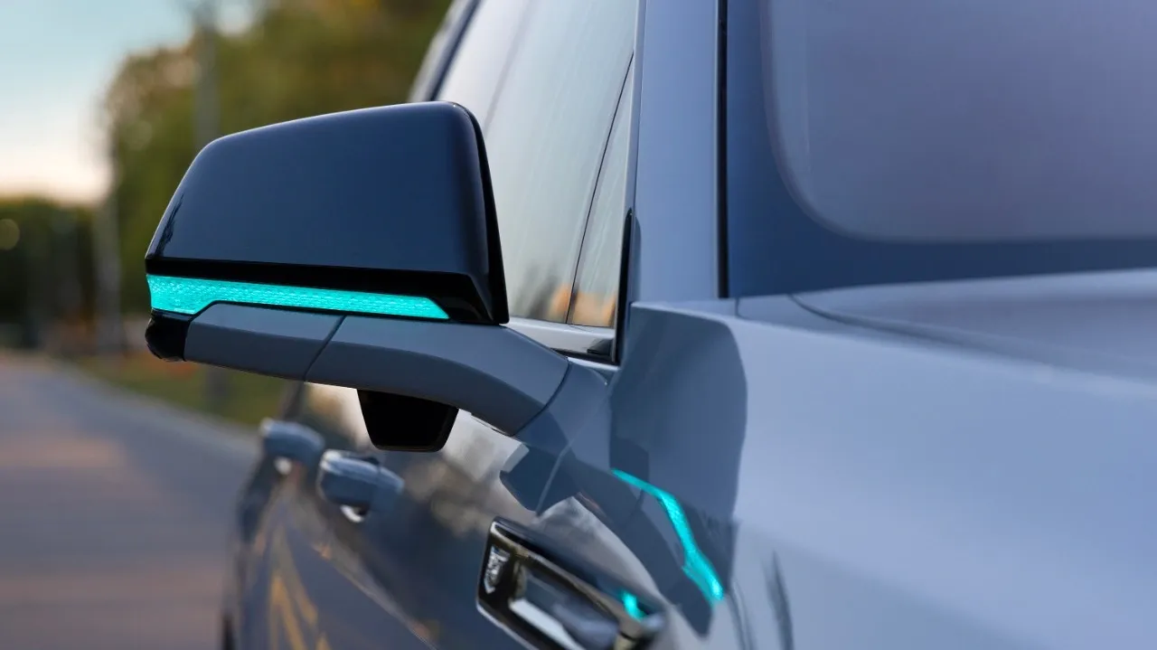Primer plano del espejo lateral de un Cadillac Escalade IQ con una franja de luz turquesa.