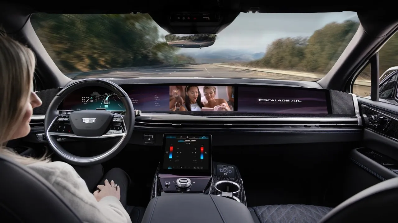 Vista del interior de un Cadillac Escalade IQL con una persona en el asiento del conductor y pantallas a lo largo del tablero.