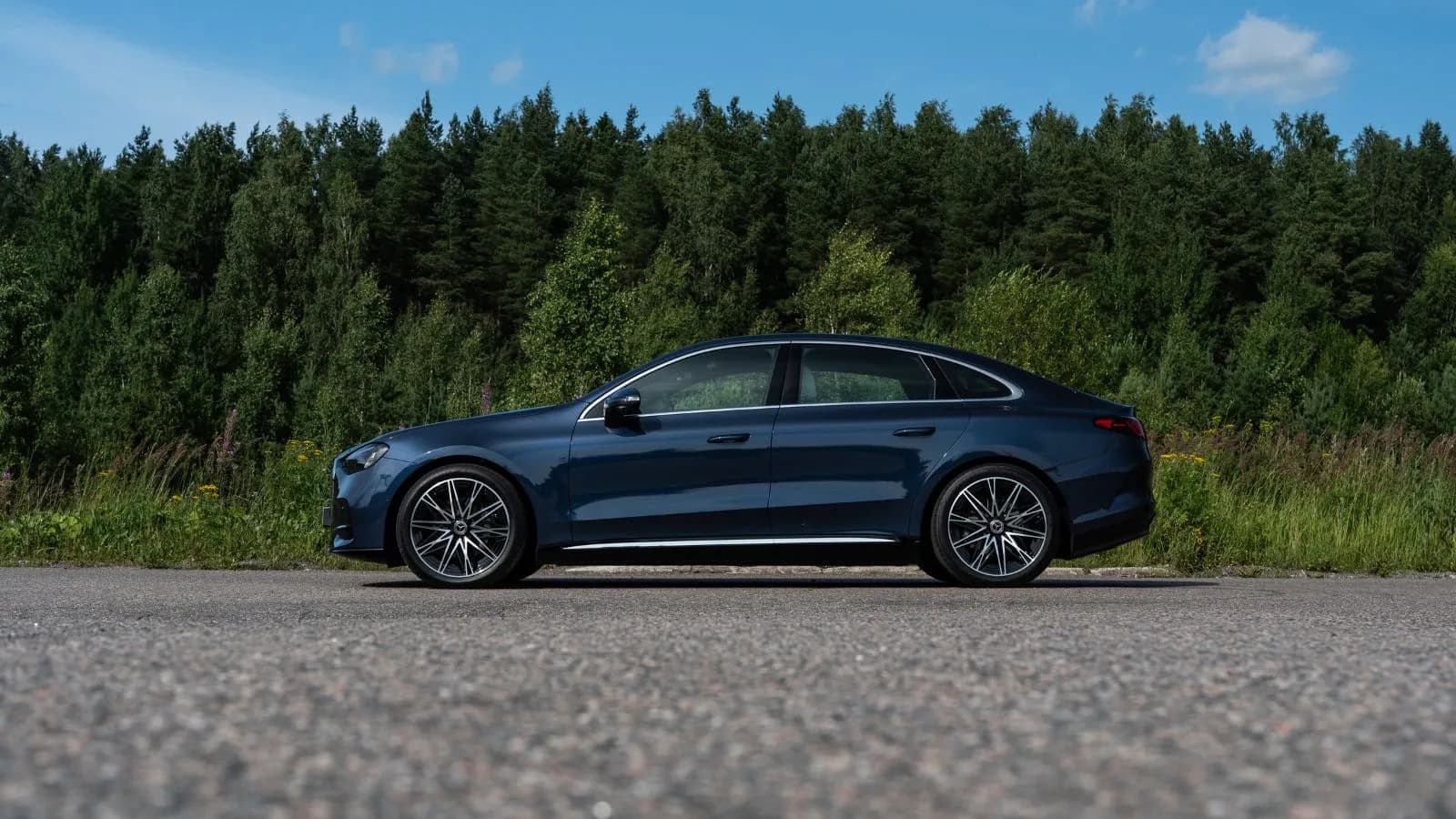 A dark blue 2027 Mercedes-Benz C400 4MATIC Electric staged in front of a dense green pine forest