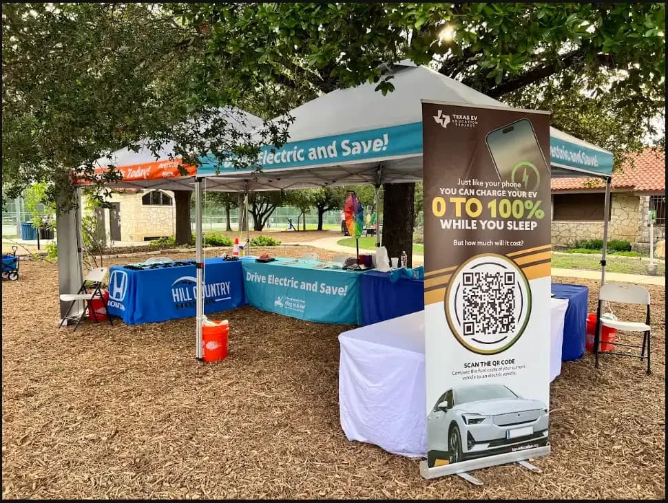 EV education booth under a tent with a QR code banner and tables.
