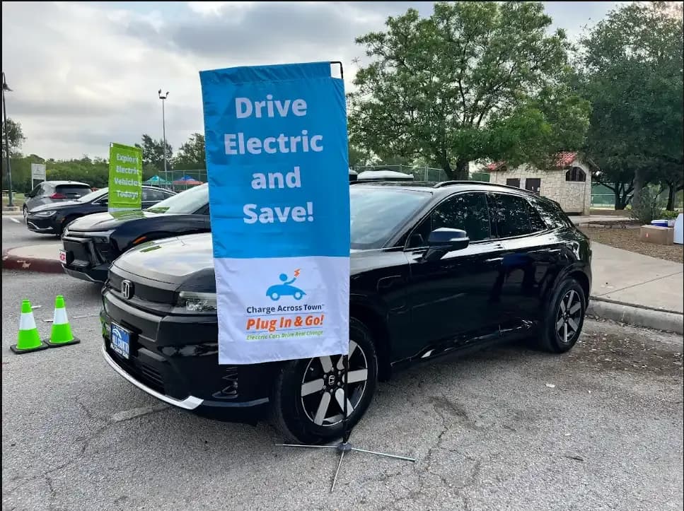 Front three-quarter view of a black Honda Prologue beside an electric-vehicle display banner.