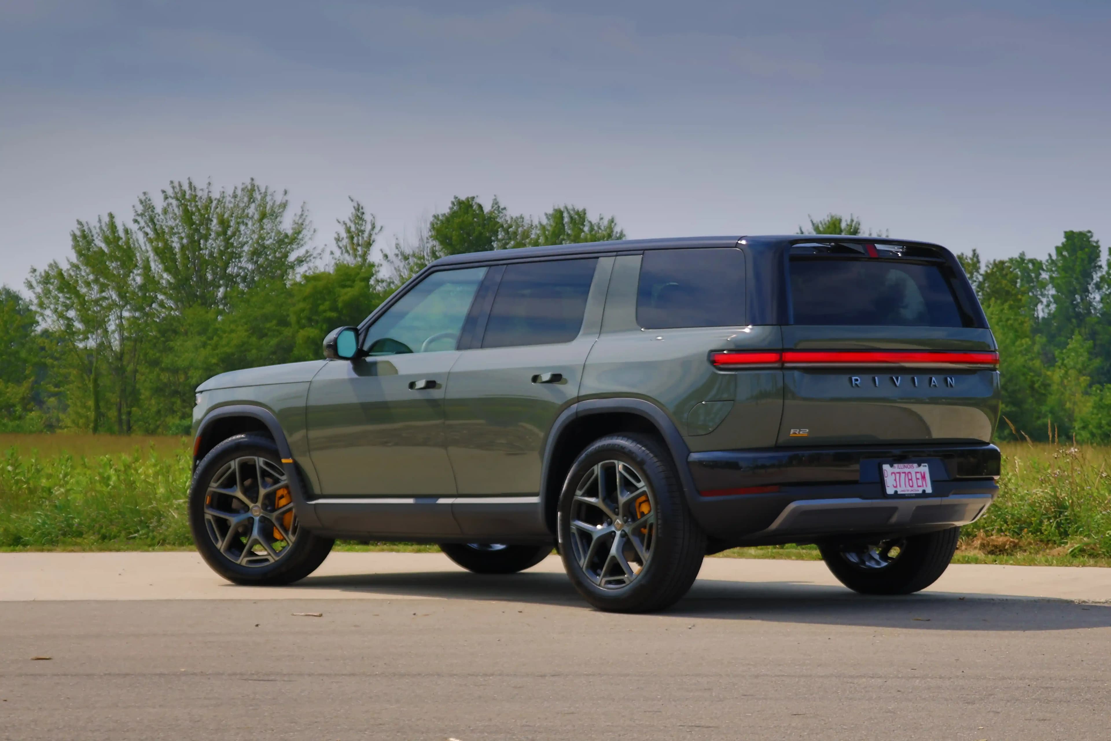 Rear three-quarter view of a Rivian R2 with flush door handles and a full-width rear light bar.