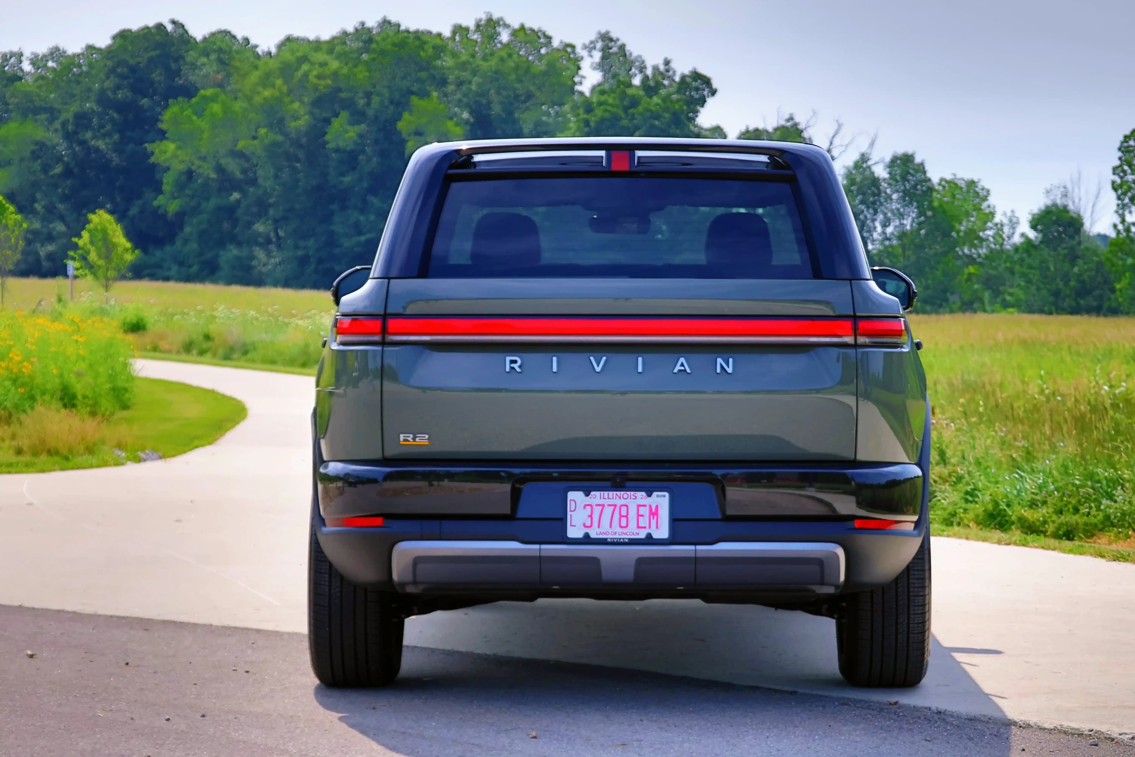 Rear view of a Rivian R2 on a winding road.