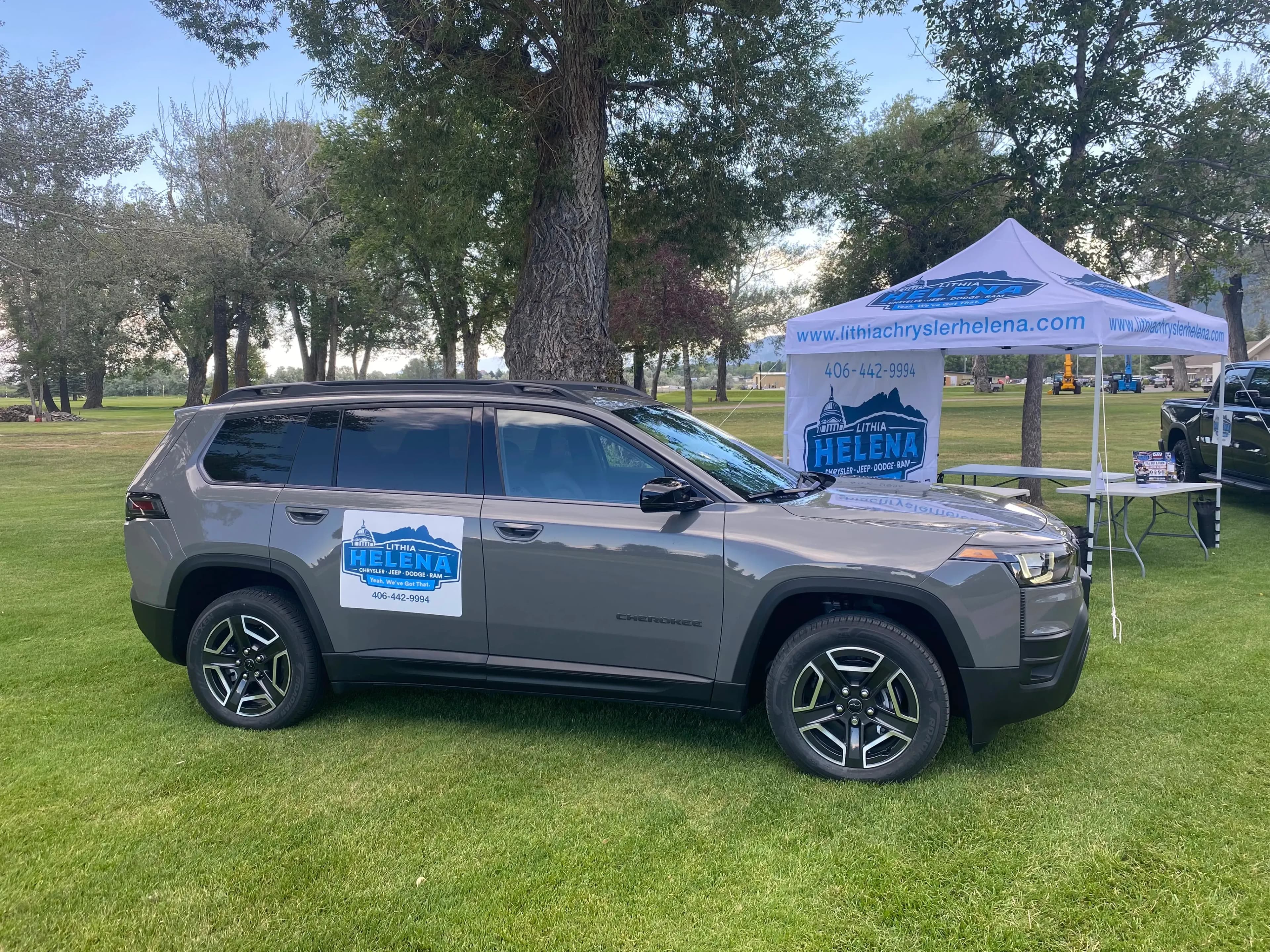 Side view of a gray Jeep Cherokee parked beside a Lithia Helena canopy tent.