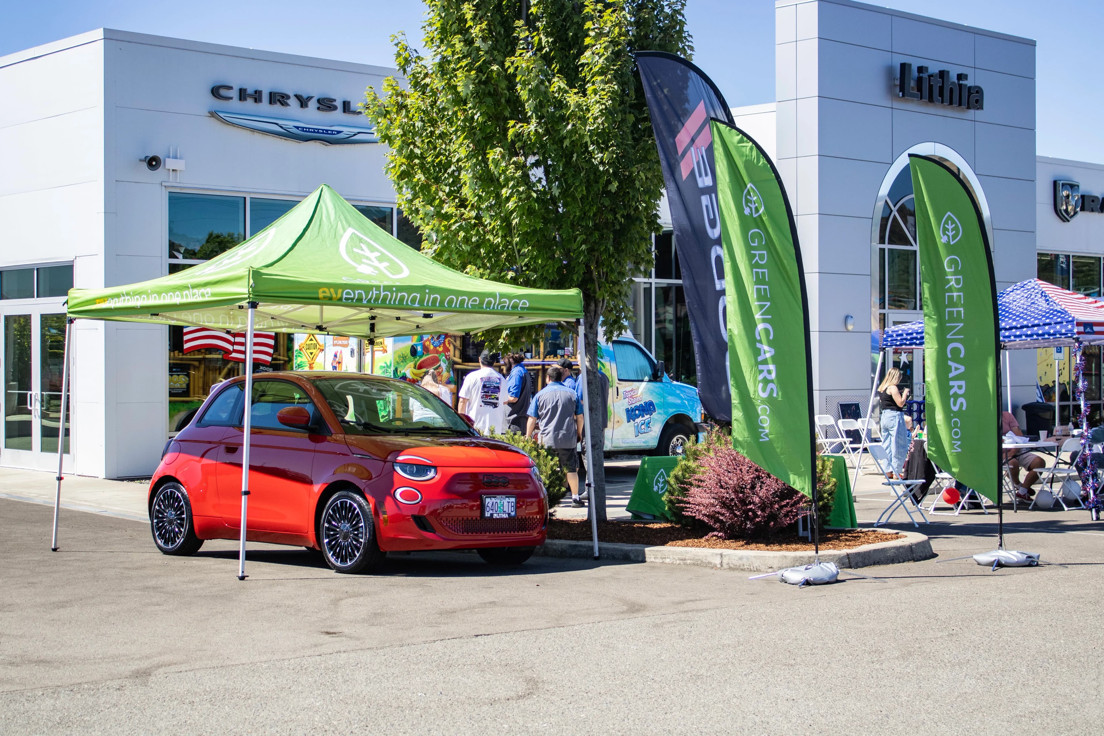 Vista frontal de un coche eléctrico compacto rojo bajo una carpa verde en un evento de concesionario.
