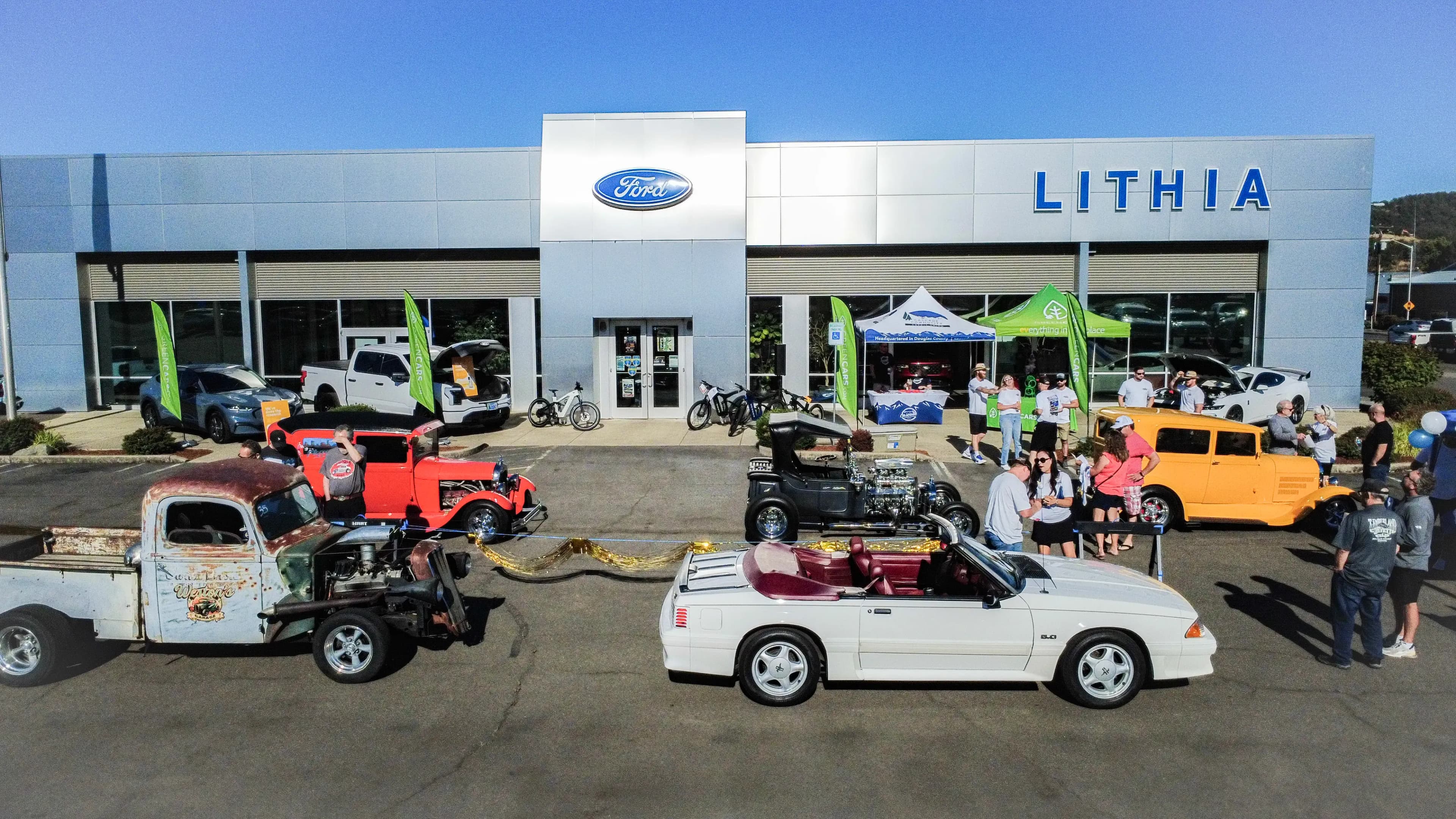 Vista amplia de autos clásicos y personas afuera de una concesionaria Lithia Ford.
