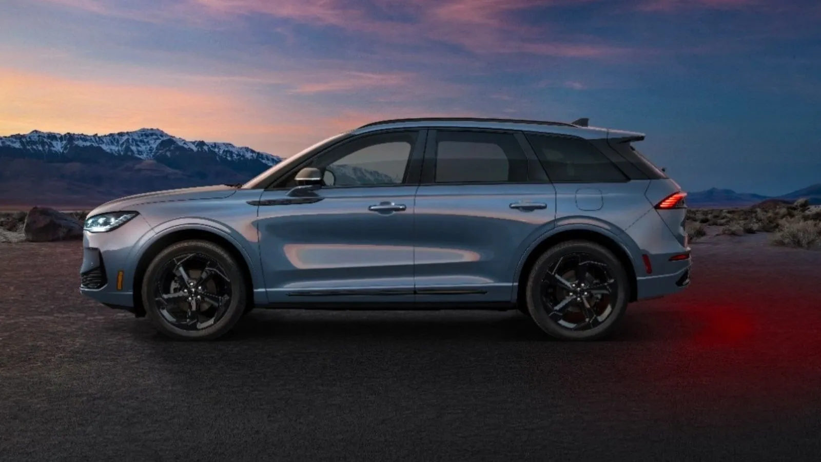 Side profile view of the 2027 Lincoln Corsair Hybrid in a silver color with mountainous terrain in the background against a sunset. 