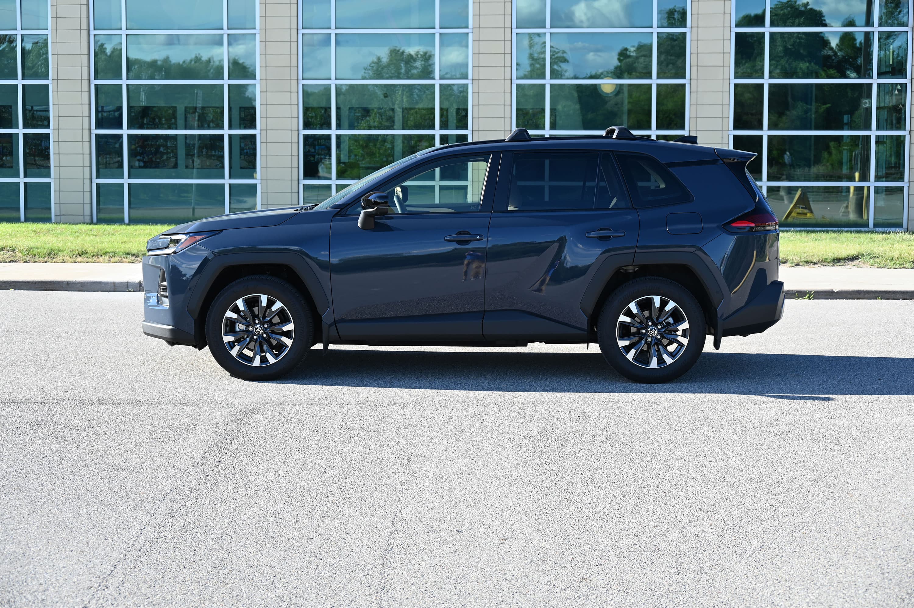 Perfil lateral de una Toyota RAV4 Hybrid azul oscuro estacionada junto a un edificio de vidrio.