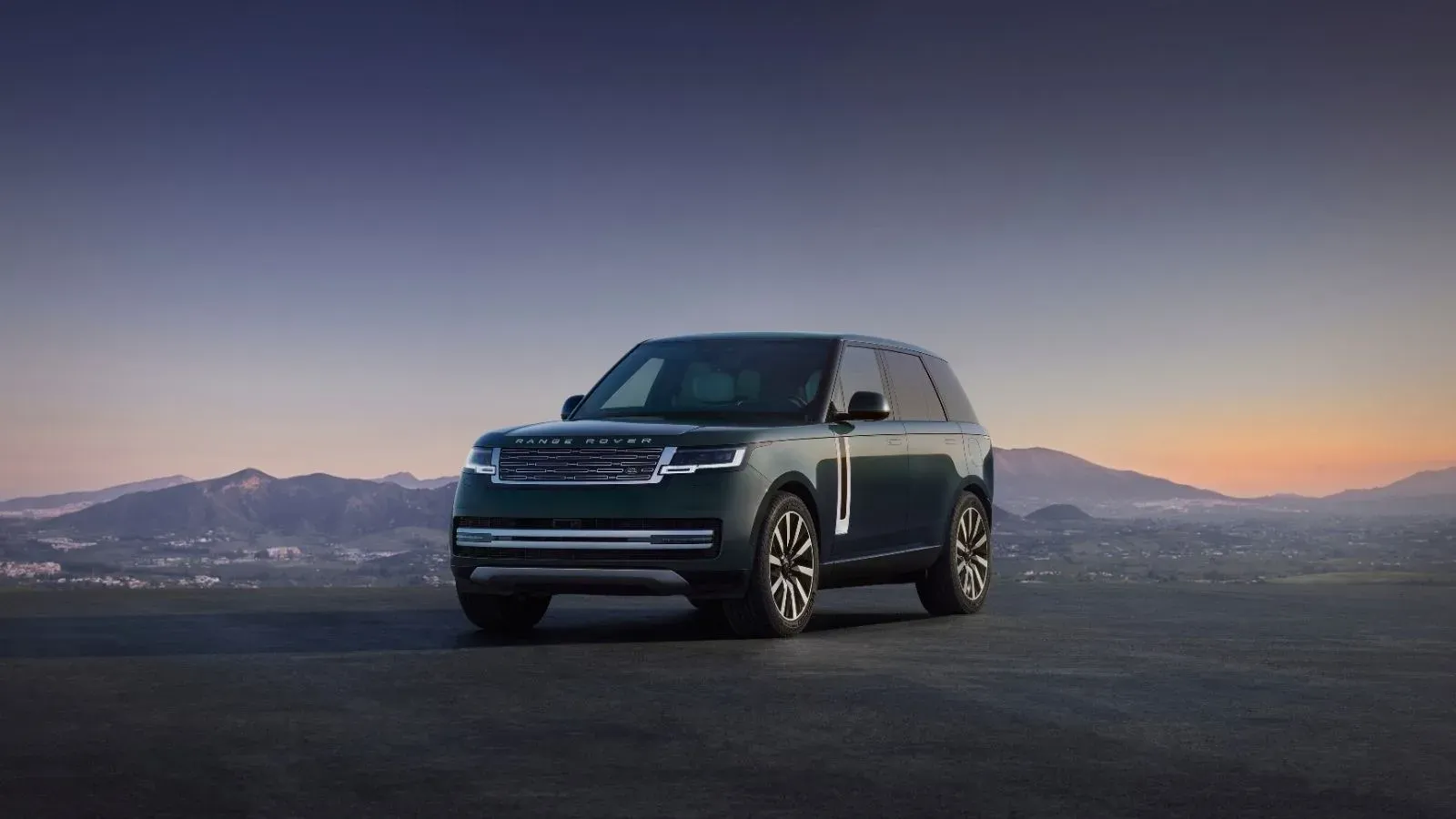 The 2027 electric Range Rover parked in front of a mountaineous terrain as the sun is rising over the horizon